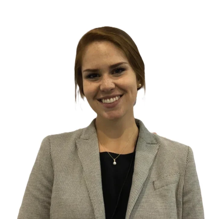 A young woman with short red hair, smiling, wearing a gray blazer and a black shirt, with a small pearl necklace and small earrings, against a white background.