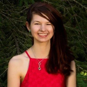 Smiling young woman with long brown hair in a red dress outdoors