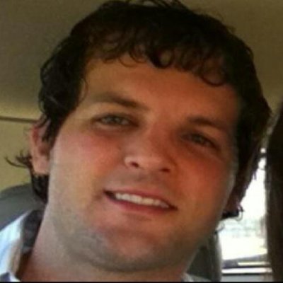 A young man with curly hair smiling inside a car.
