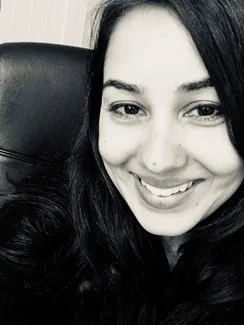 A black and white photo of a smiling woman with long dark hair, sitting in a chair.