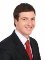 A young man in a suit and red tie smiling at the camera.