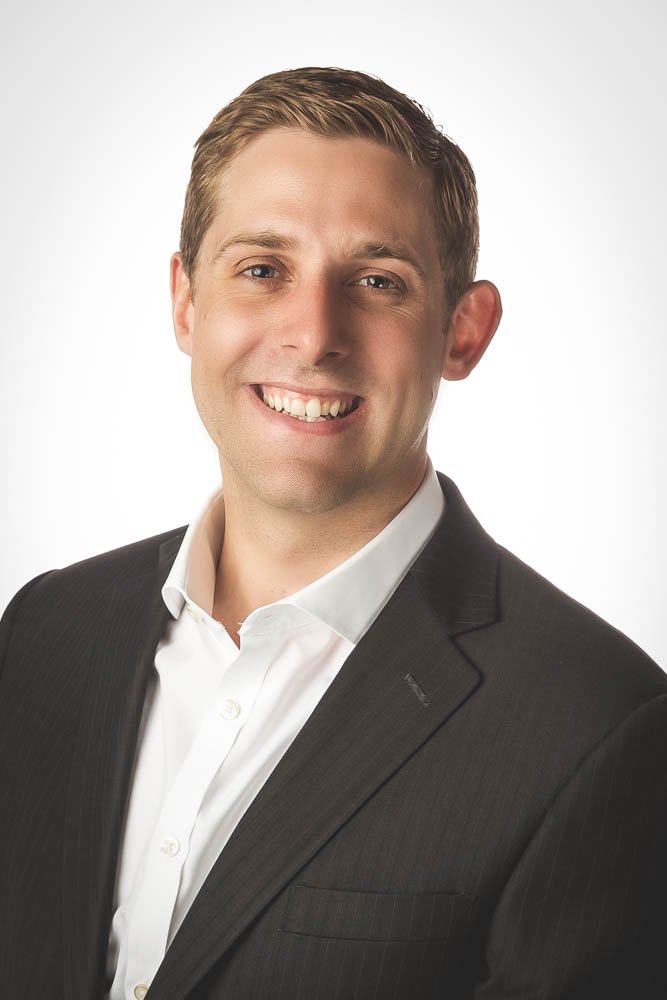 Portrait of a smiling man wearing a black suit and white dress shirt against a white background.