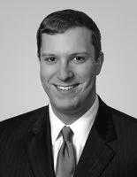 Black-and-white headshot of a young man in a suit and tie, smiling.