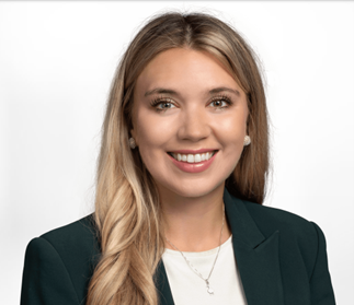 A smiling young woman with long blonde hair, wearing a dark blazer and earrings, against a plain white background.