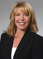 A woman with blonde hair wearing a black blazer and white top, smiling.