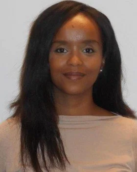 A woman with long dark hair, wearing a light beige top, looking at the camera with a slight smile.
