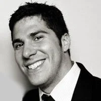 A young man with dark hair and a bright smile, wearing a tuxedo and tie, in black and white.