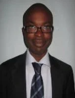 Portrait of a man in a suit and tie, wearing glasses, smiling against a neutral background.