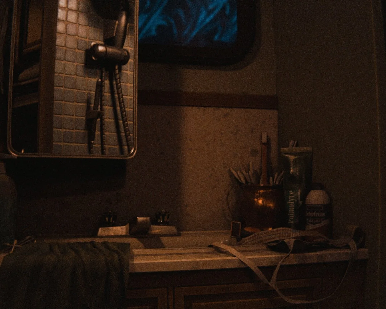 A dimly lit room with a mirror reflecting a camera on a tripod, a shelf with sunglasses, and a countertop with various objects including a copper container filled with tools, a thermos, and miscellaneous items.