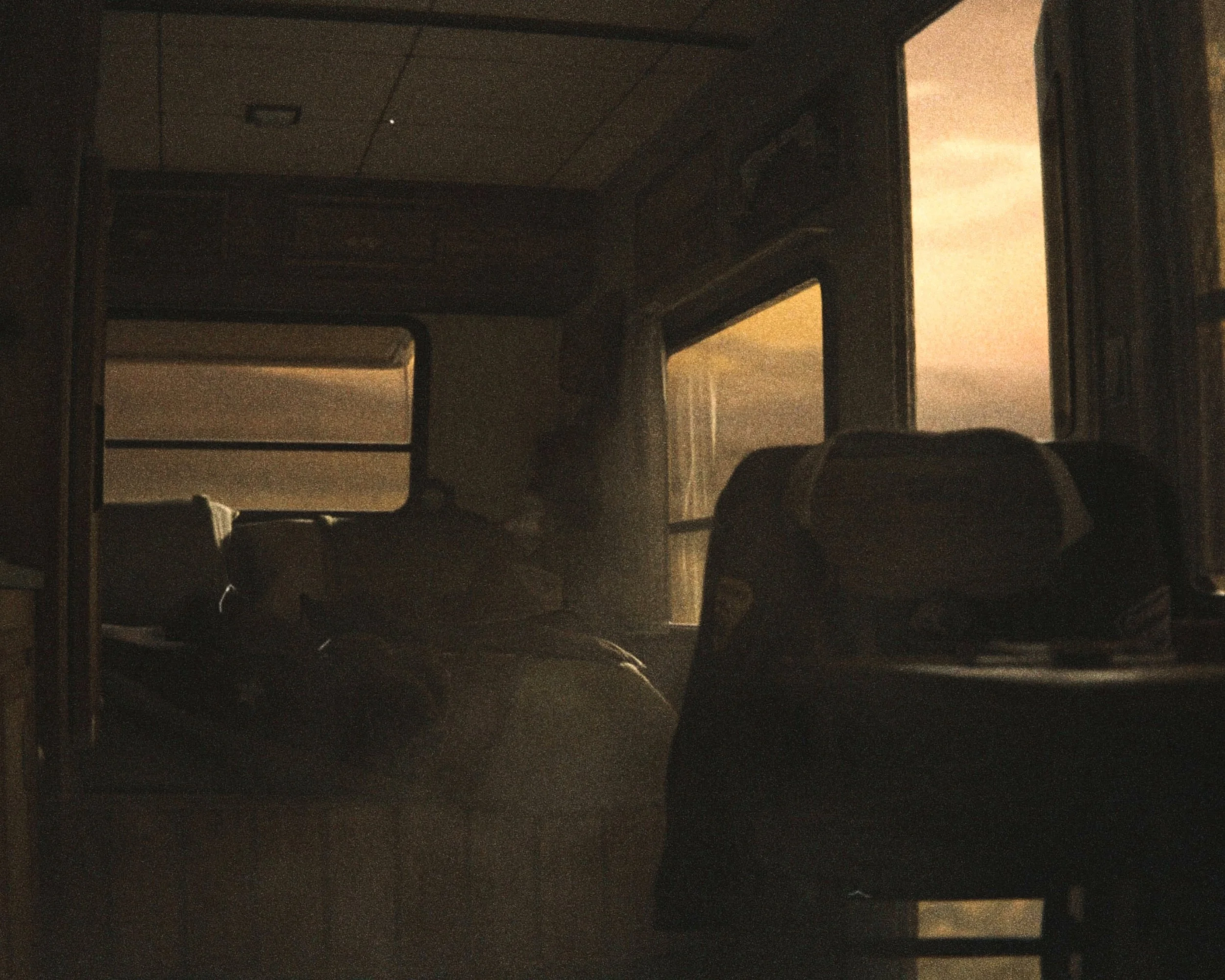 The image shows a dark, dimly lit room with a doorway opening to a brighter area outside. There are some objects, possibly furniture, visible in the foreground and background, but details are unclear due to the low lighting.