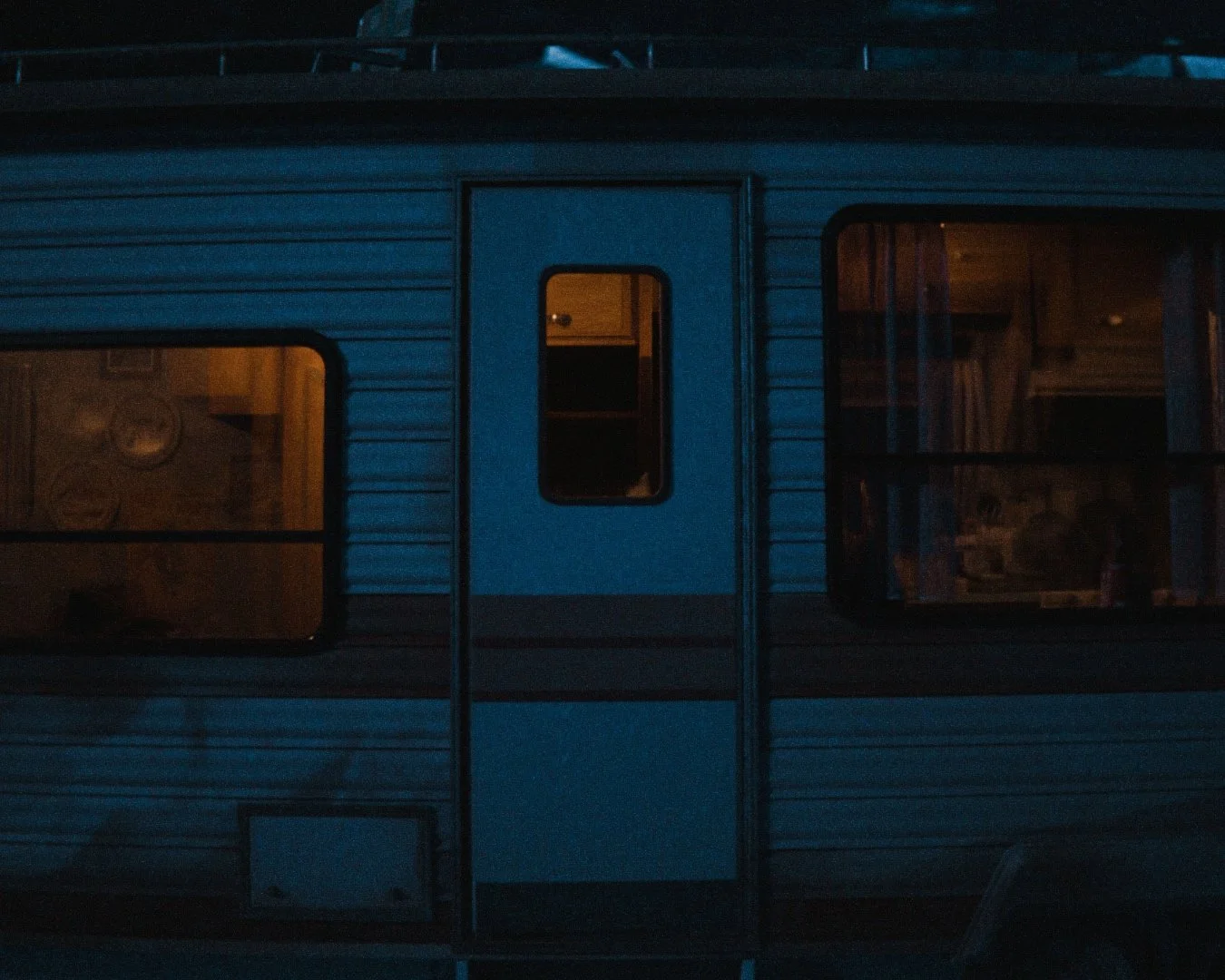 A dark, nighttime view of a camper trailer with windows showing warm indoor lighting.