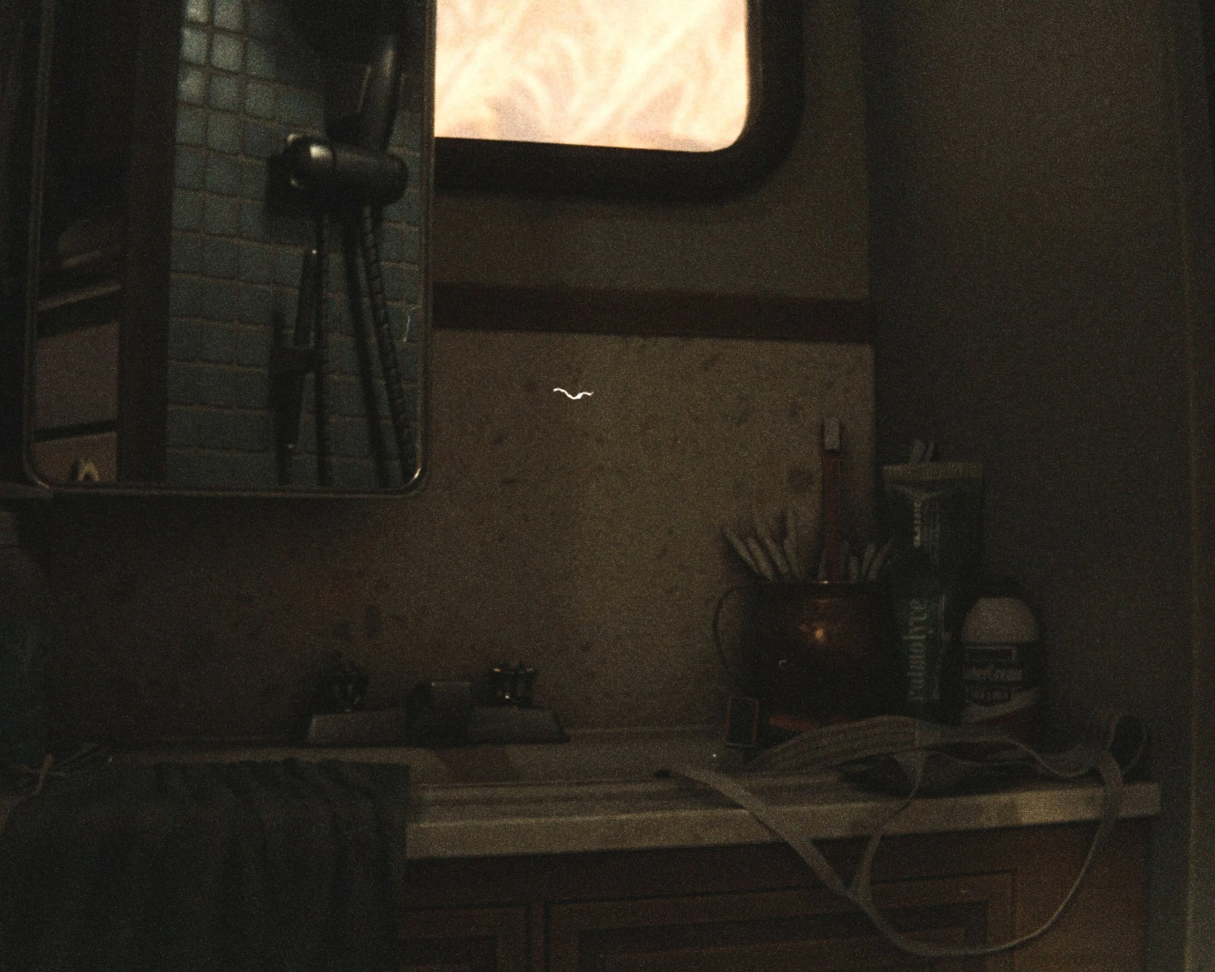 A microwave oven showing a reflection of a smartphone camera and part of the room in a dimly lit kitchen.