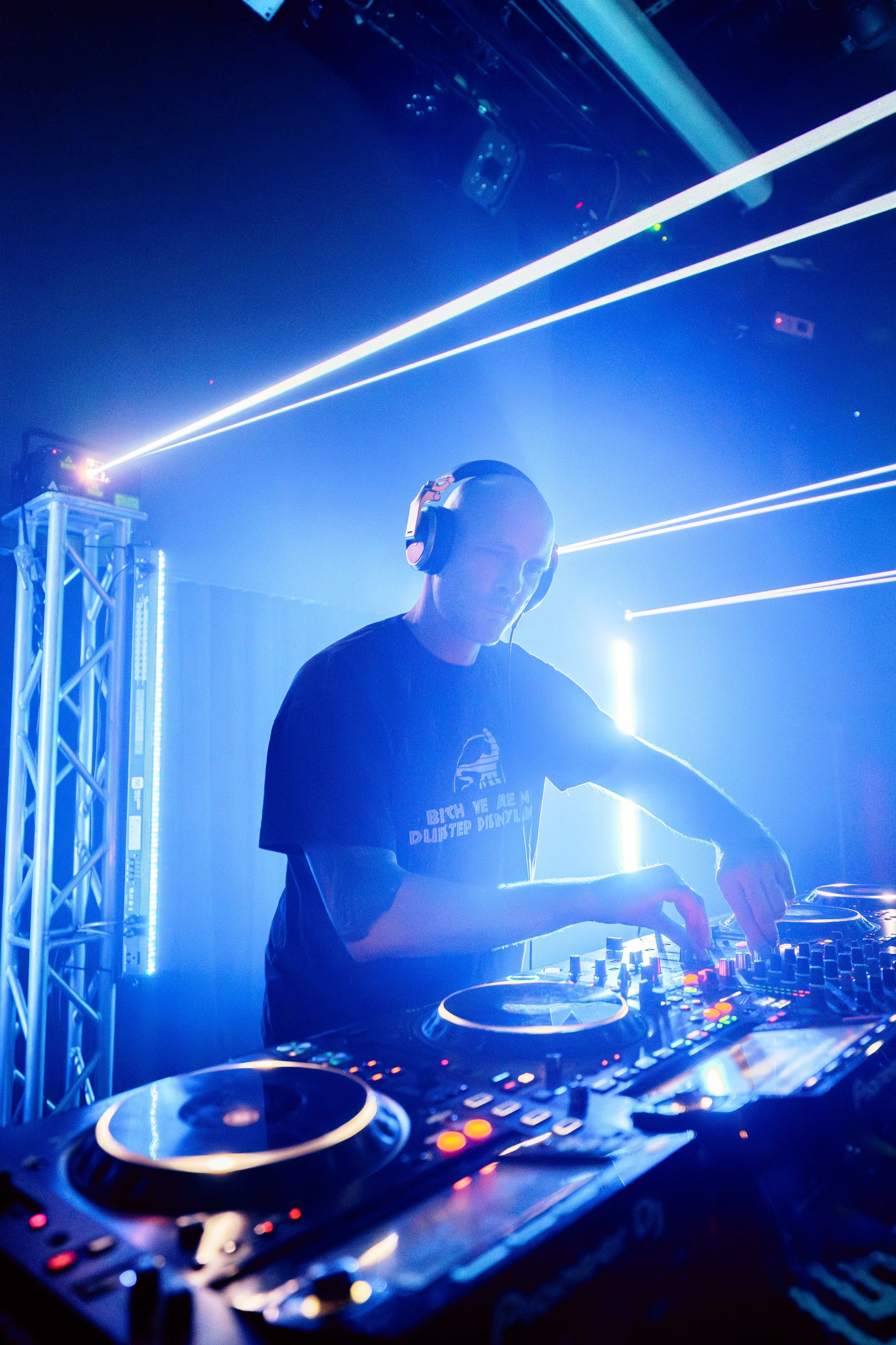 DJ performing at a nightclub with blue lighting and laser lights in the background.