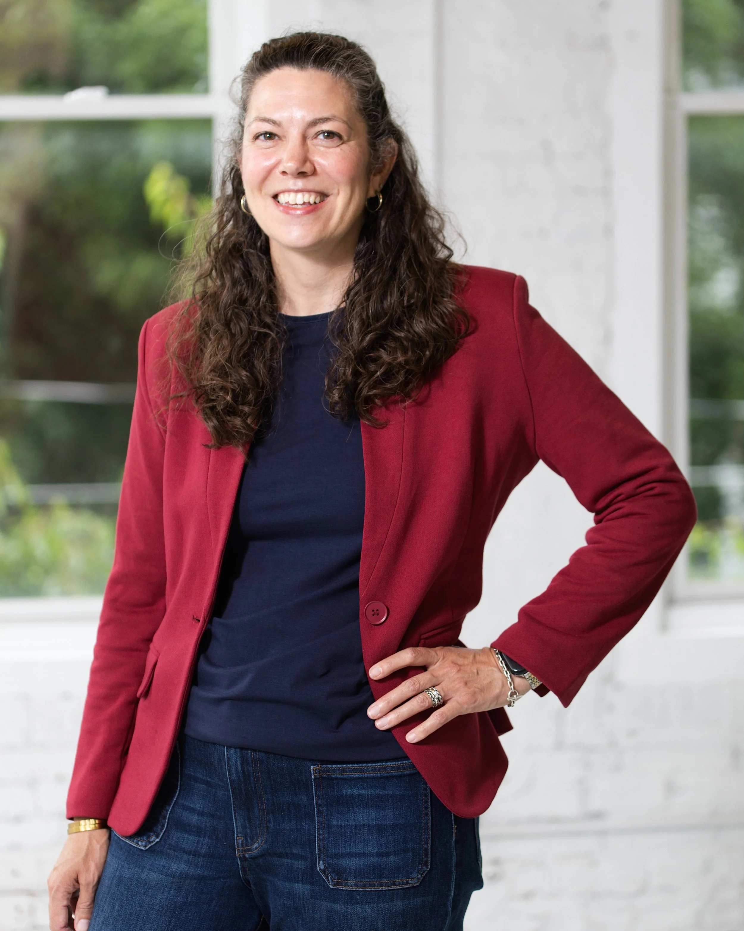 Katie Chew smiling at the camera wearing a burgundy blazer and navy shirt indoors