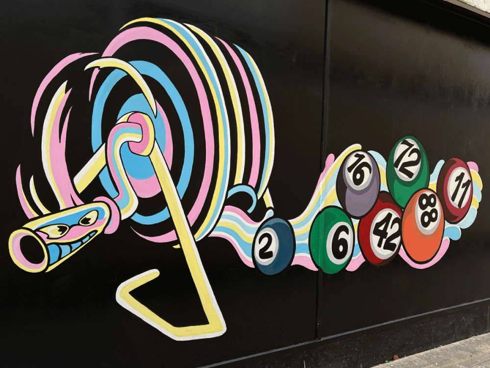 Colourful graffiti mural of a cartoon-style bingo spinner with a rainbow colours, with numbered bingo balls spilling out on a black wall.