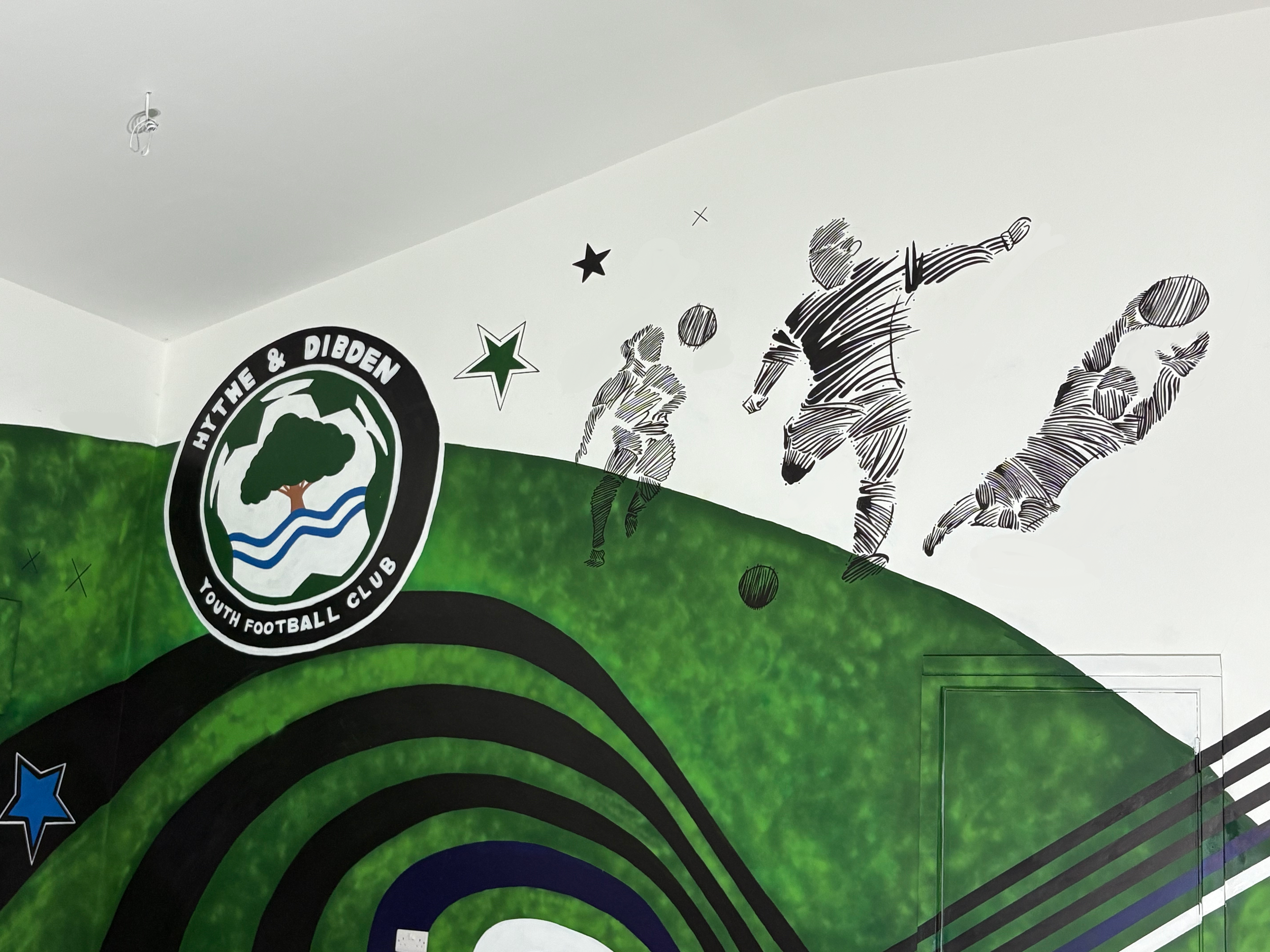 A mural featuring children playing soccer, with the logo of a youth football club and various star designs on a green background.