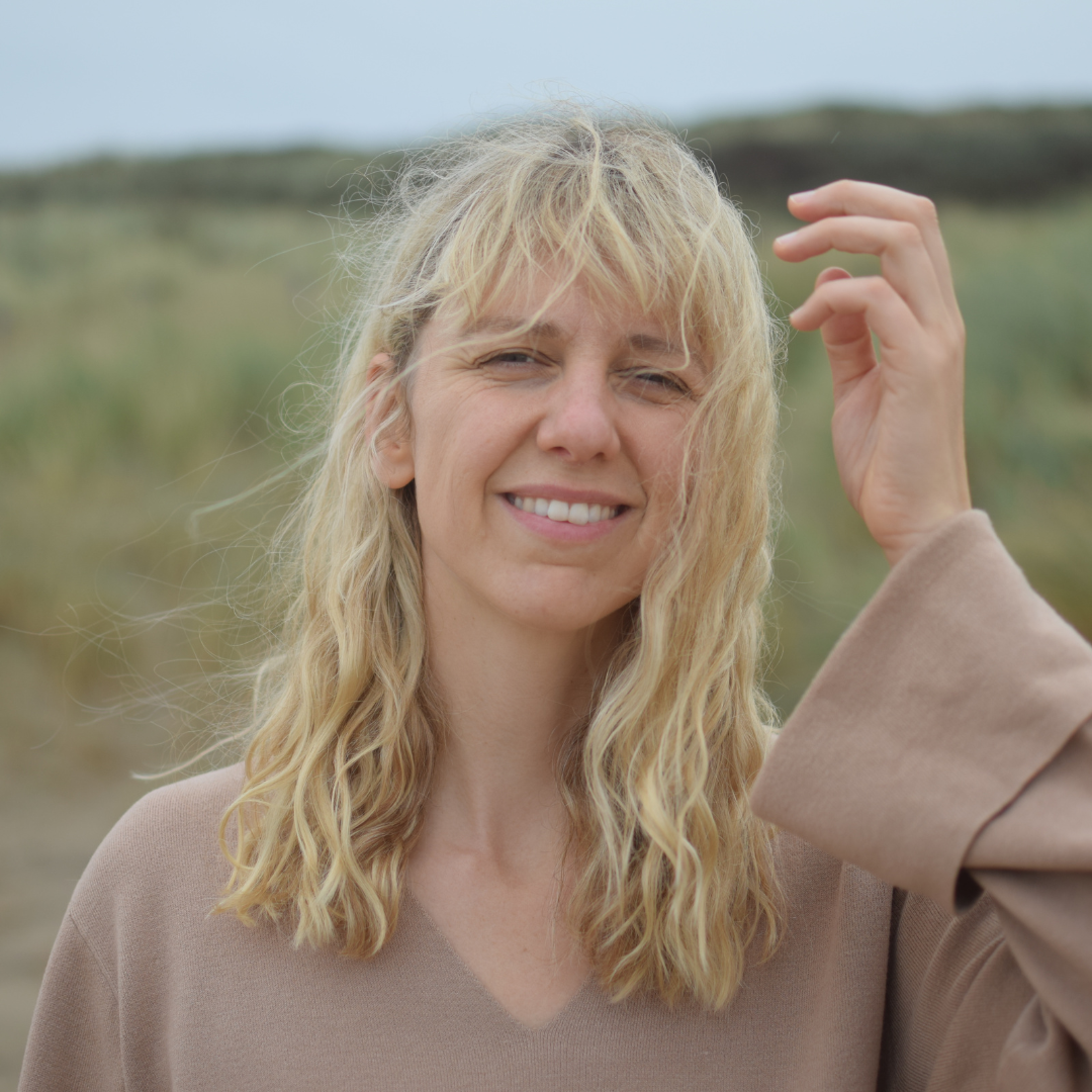 Person with long blond hair smiling outdoors