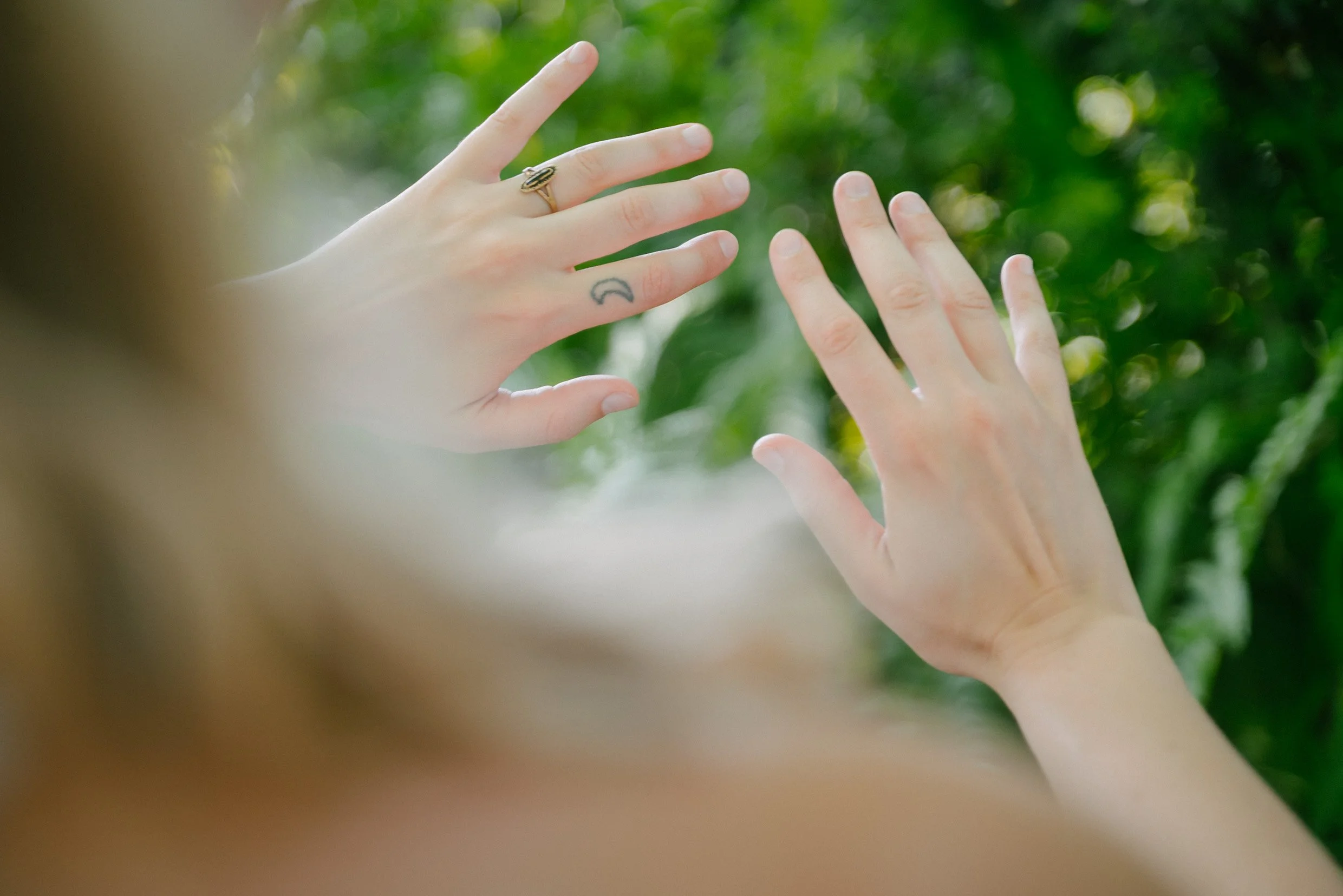 Two hands with rings and a tattoo against a blurred green background.