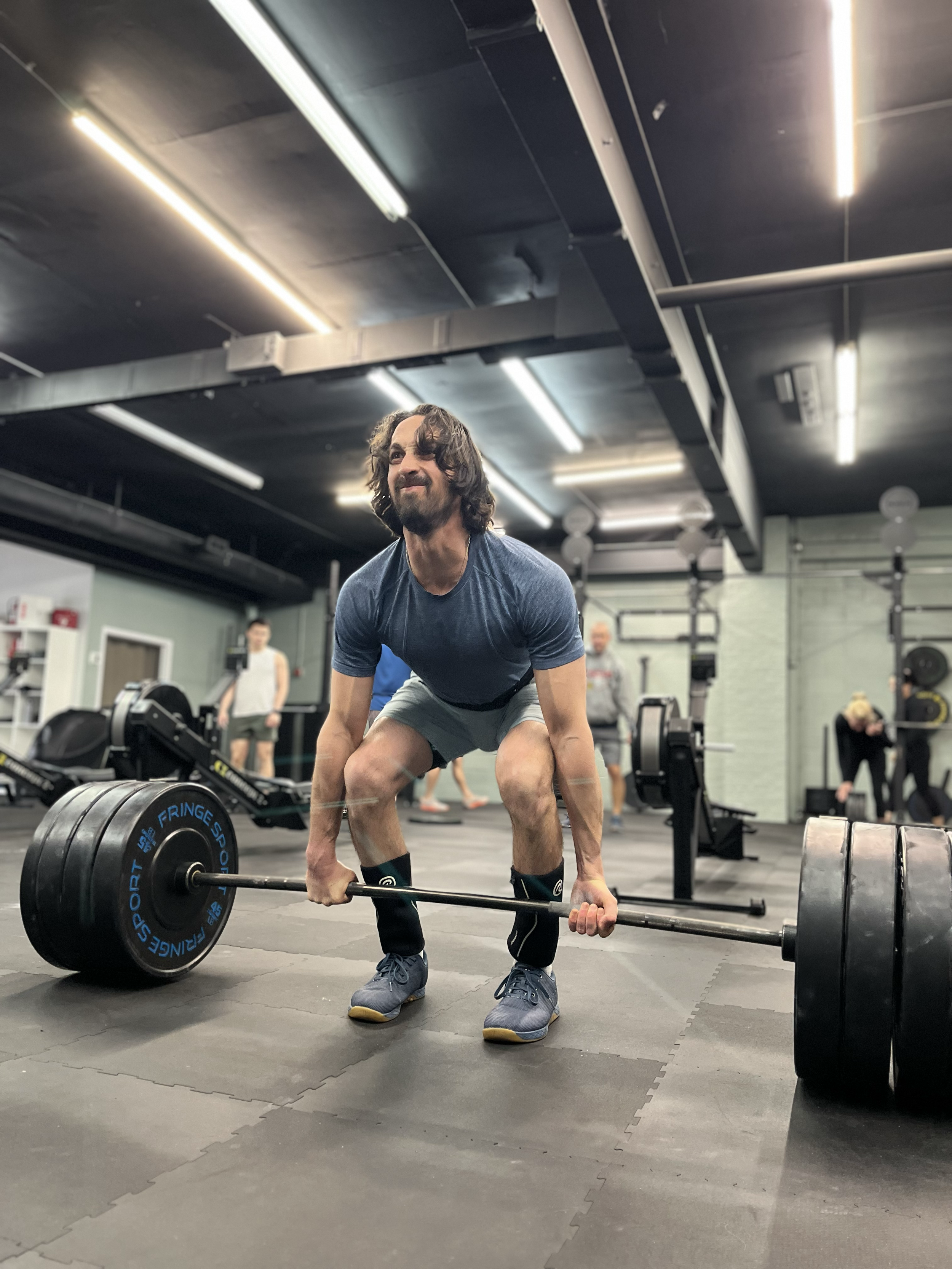 A man with long hair and a beard lifting a heavy barbell in a gym.