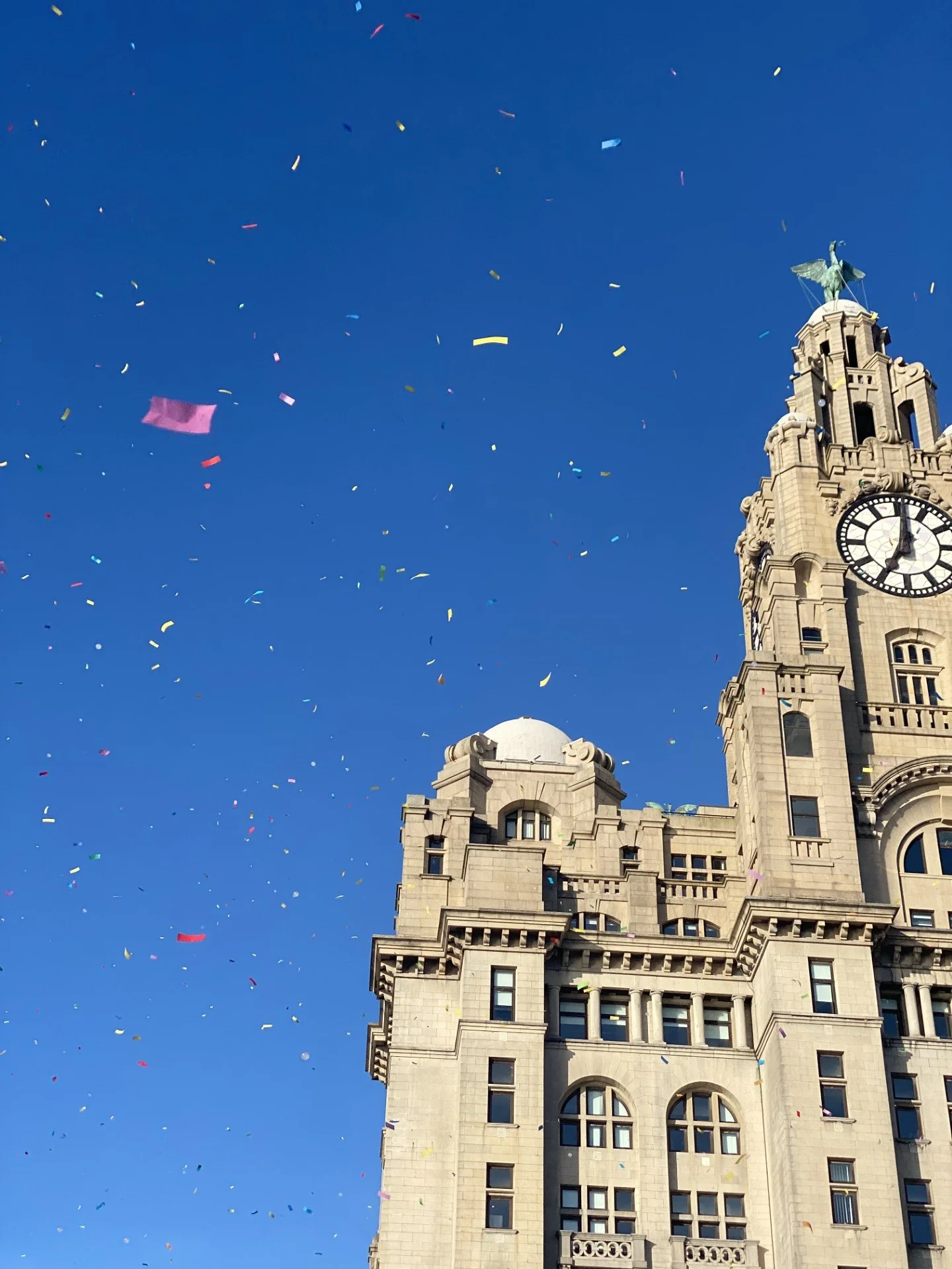 The Liver Building - a historic building in Liverpool with a clock tower under a blue sky, with colourful confetti falling.