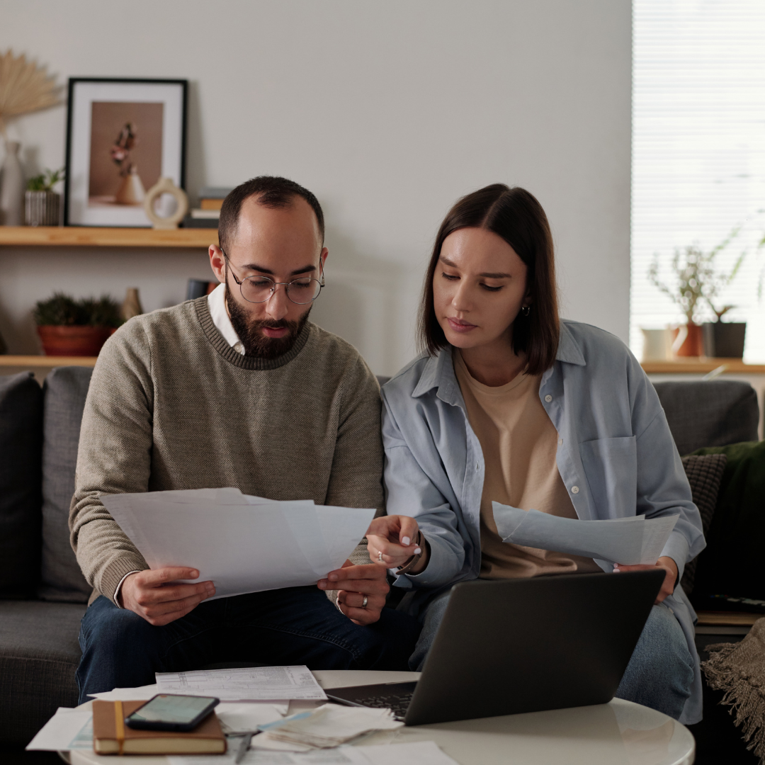 A couple sitting together on a sofa, reviewing paperwork and a laptop