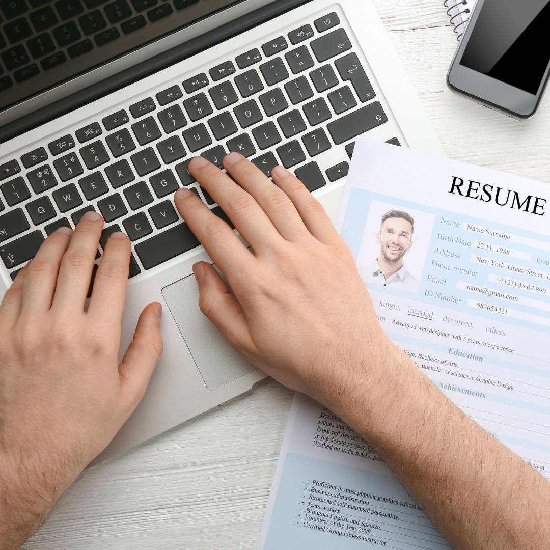 Hands typing on a laptop beside a printed resume
