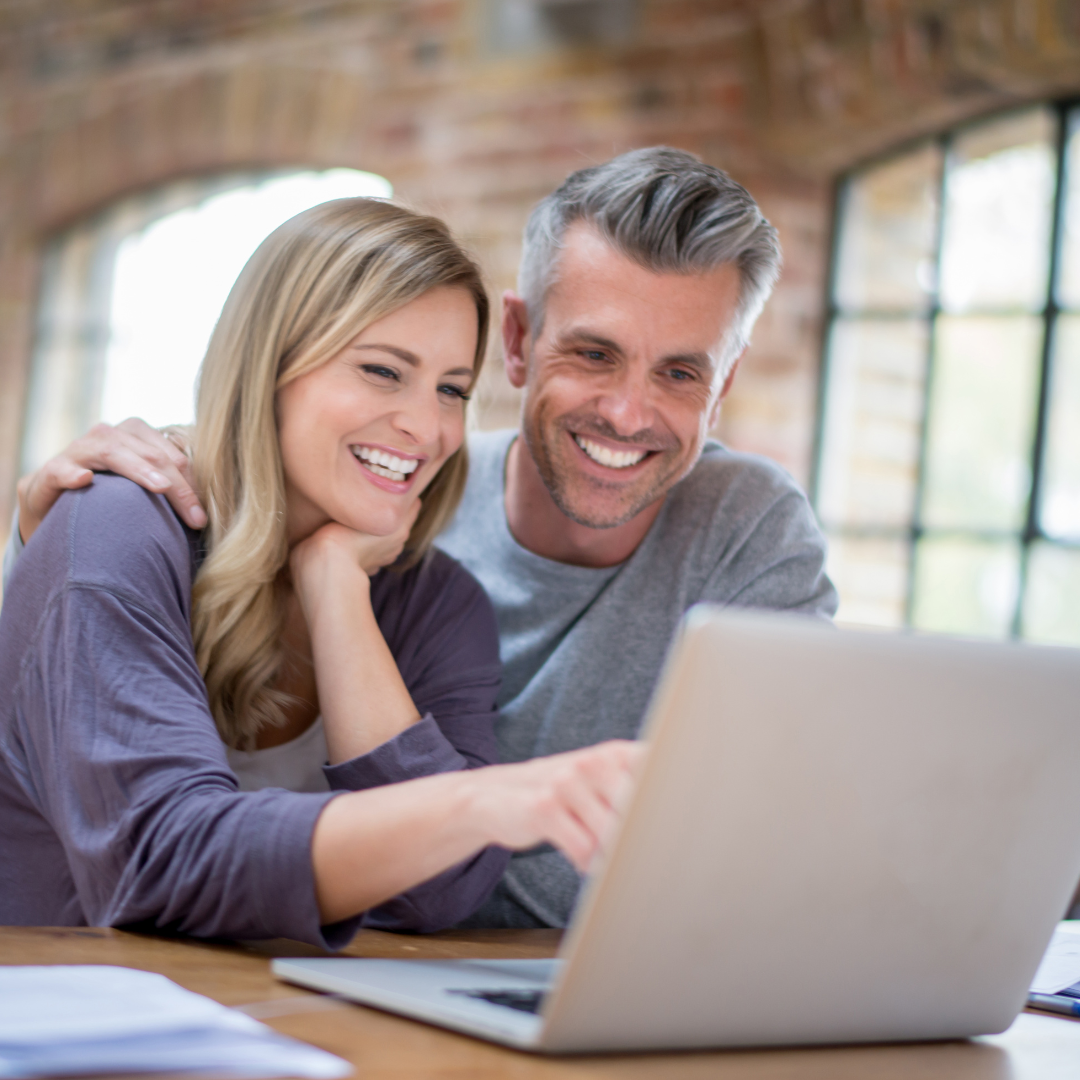 A smiling couple sitting close together, looking at a laptop