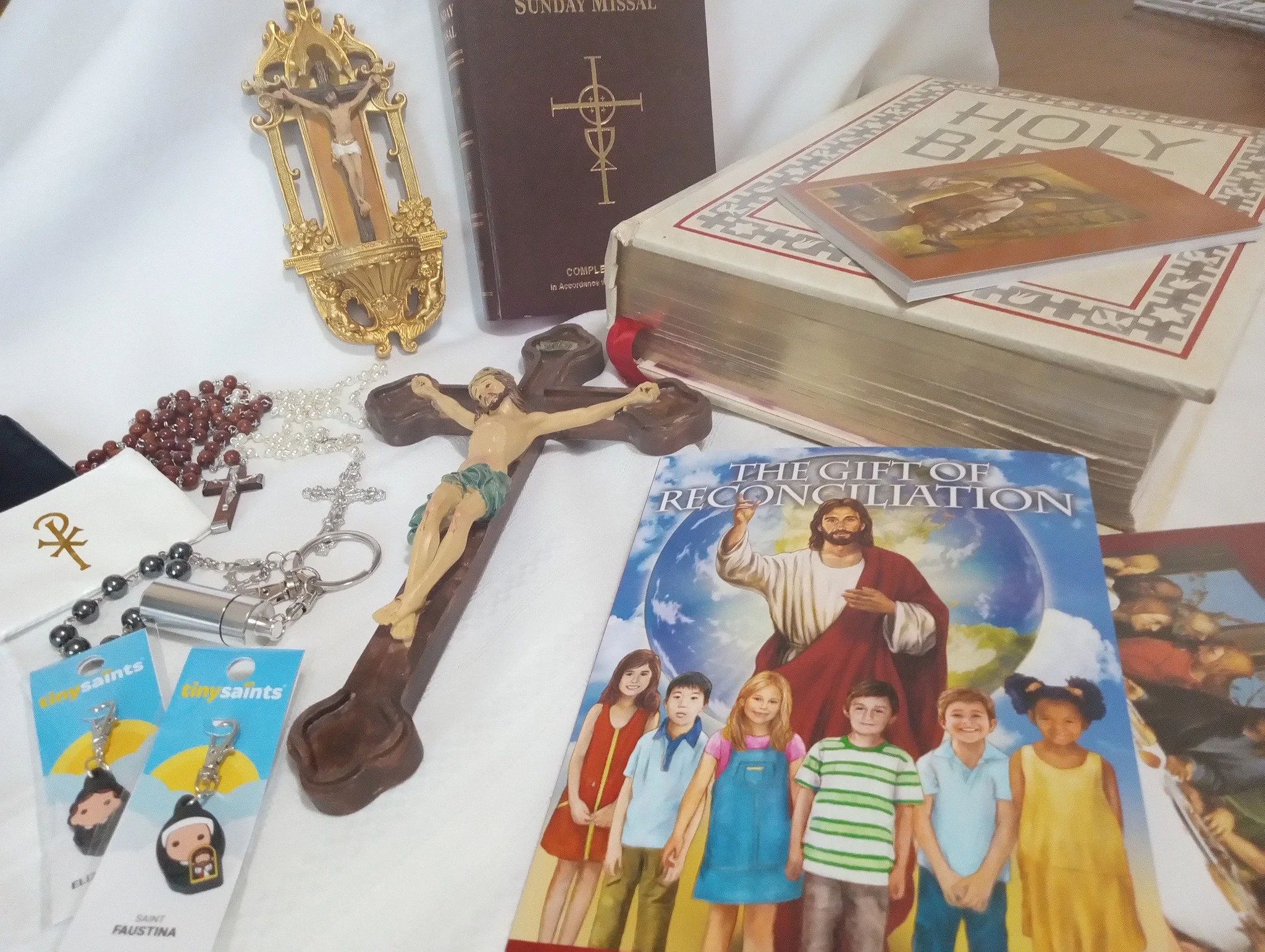 Religious items for children, including a crucifix, a Bible, a book titled "Sunday Missal," rosary beads, colorful prayer cards, a booklet titled "The Gift of Reconciliation," and a photo of Jesus Christ with children.