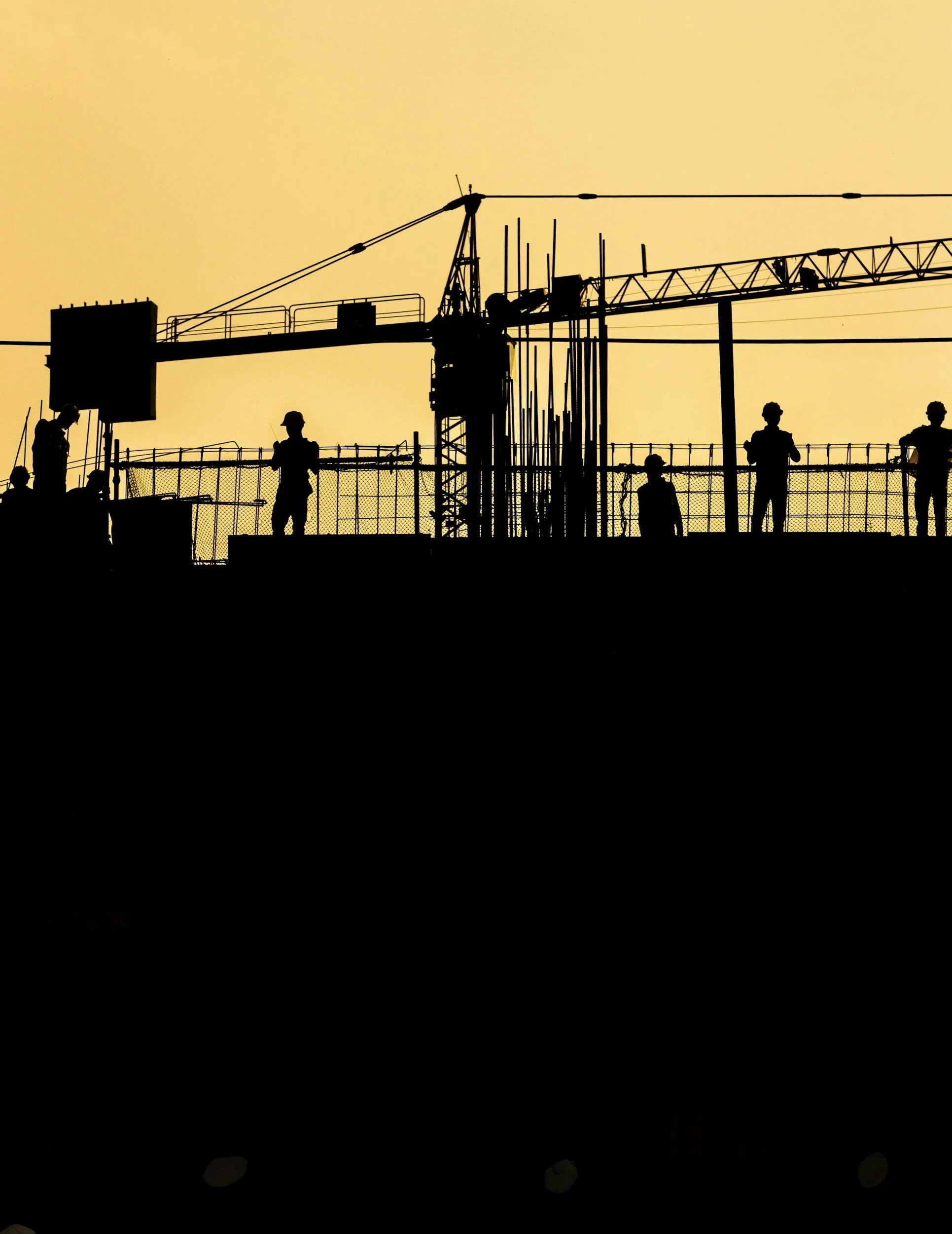 Silhouettes of construction workers and a tower crane on a construction site at sunset or sunrise.