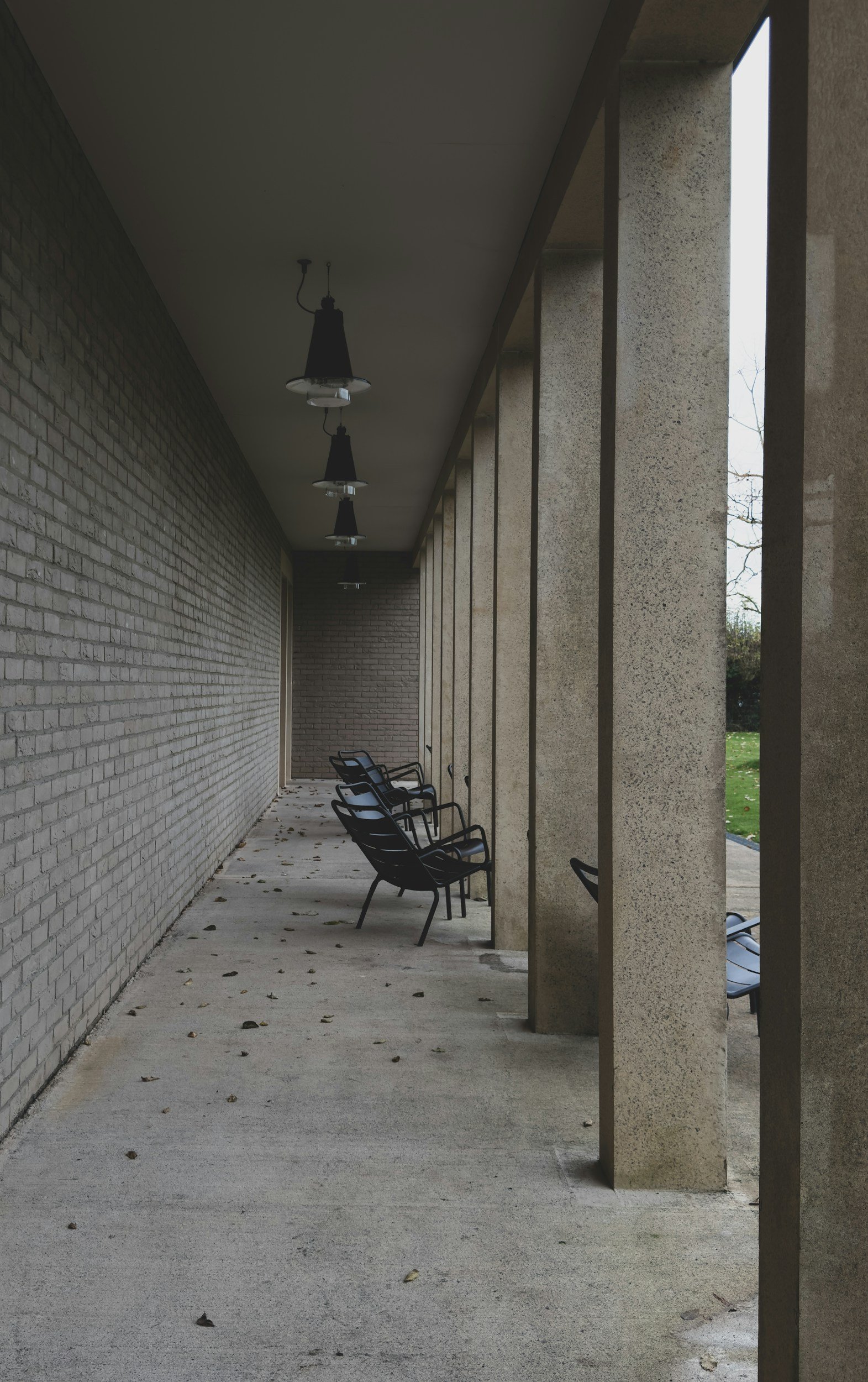 Empty bench seating area with brick wall and concrete pillars outside, overcast sky.