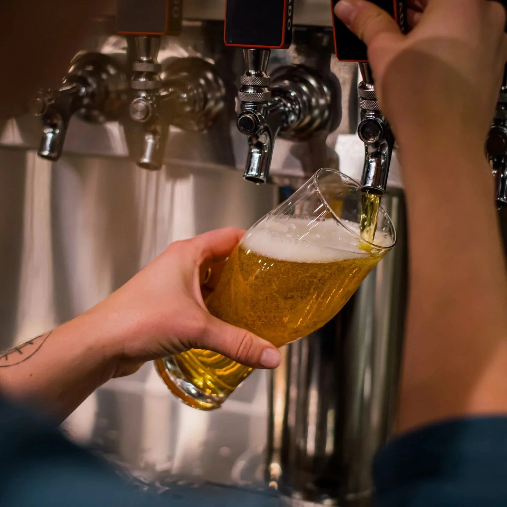 A person fills a pint glass with beer from a tap at a bar or brewery.