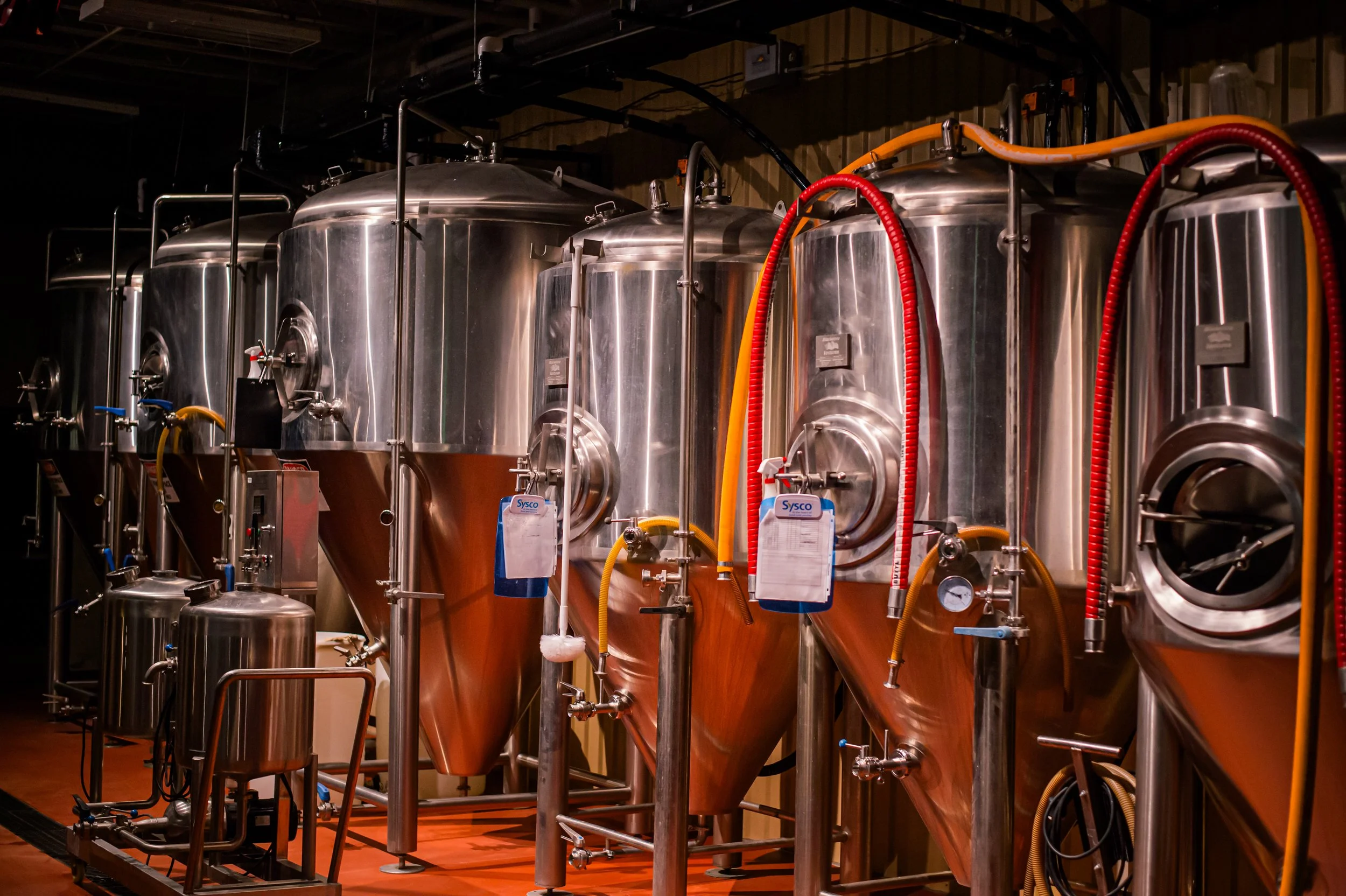 Industrial brewing tanks or fermenters made of metal, with connected pipes and gauges, in a brewery or laboratory setting.