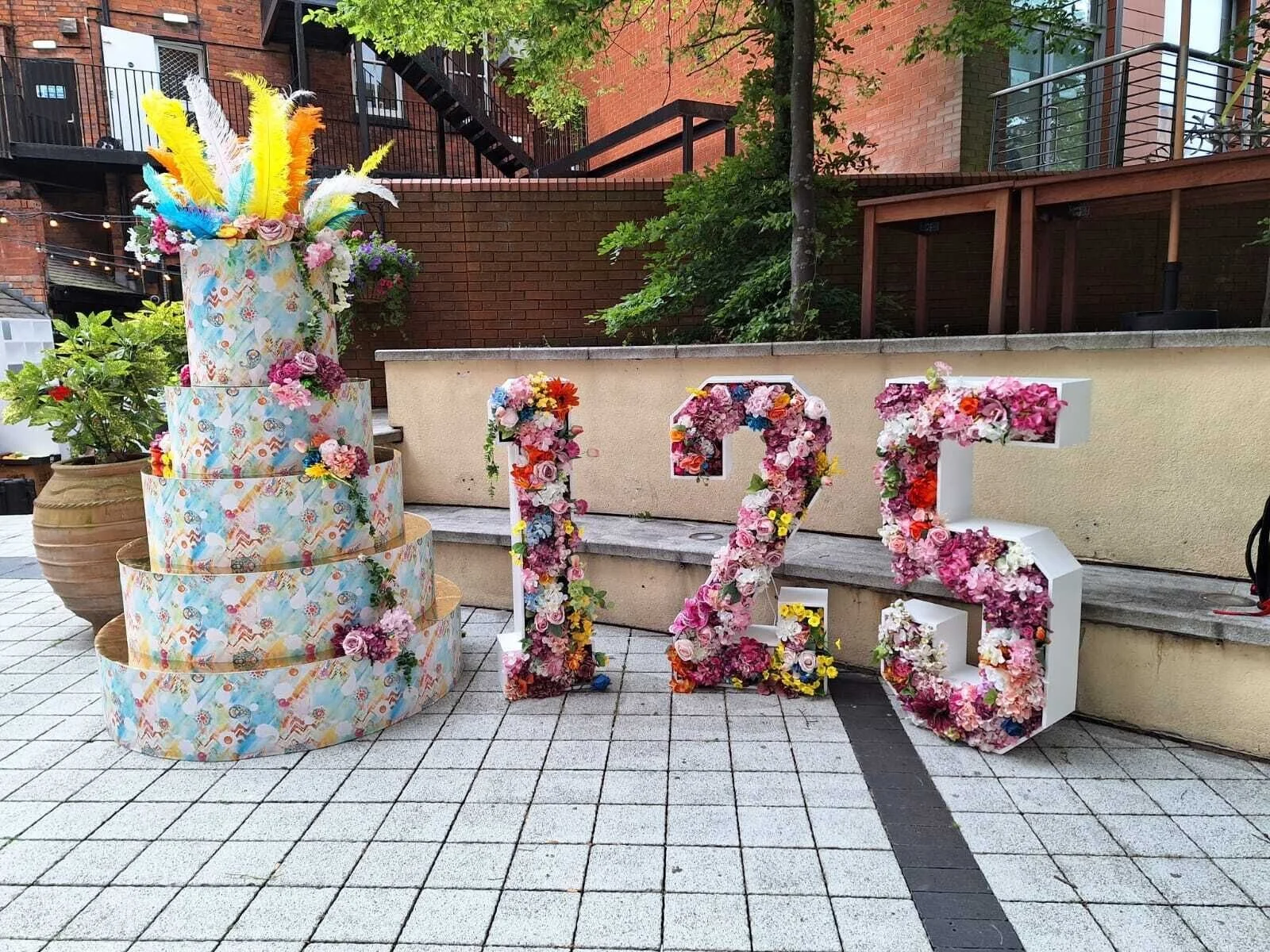 Colorful floral decorations spelling out the number 13 to celebrate a birthday or special occasion, with a tiered cake decorated with feathers and flowers beside them.
