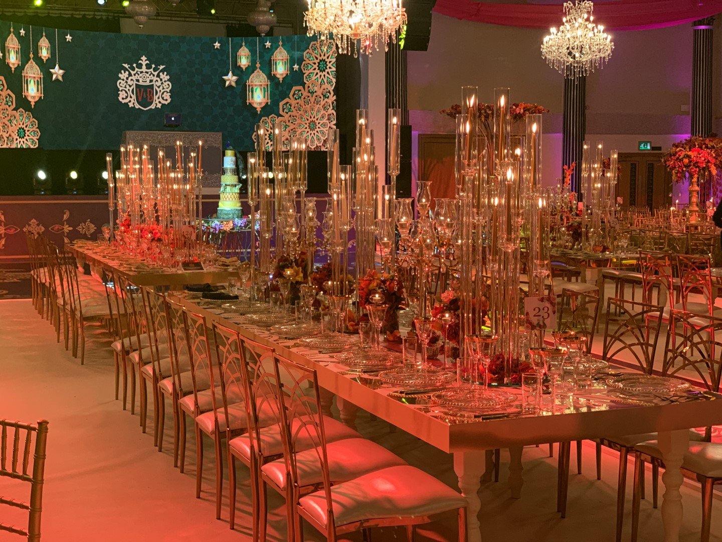 Elegant banquet hall decorated with tall candleholders, floral centerpieces, chandeliers, and colorful lighting for a formal celebration or wedding reception.