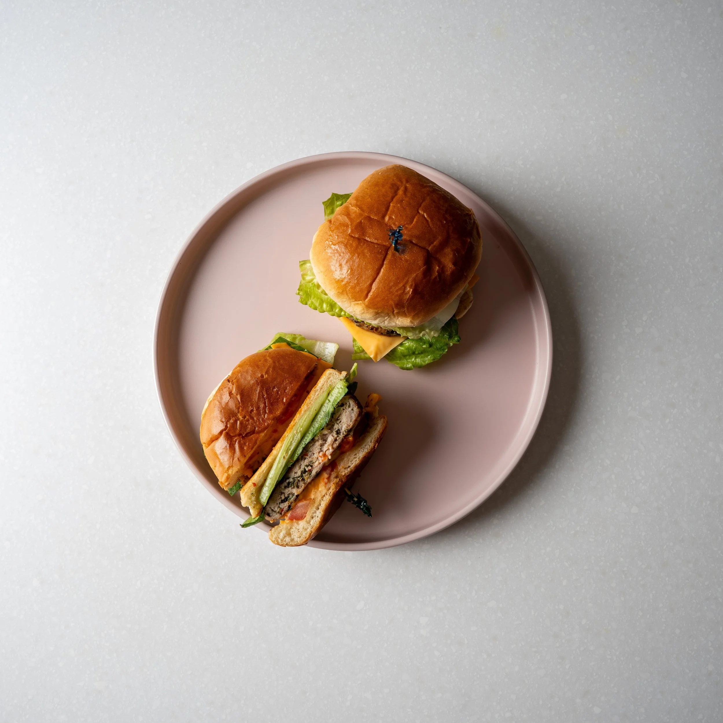pink plate with two small sliders, one is cut in half showing a seared beef patty