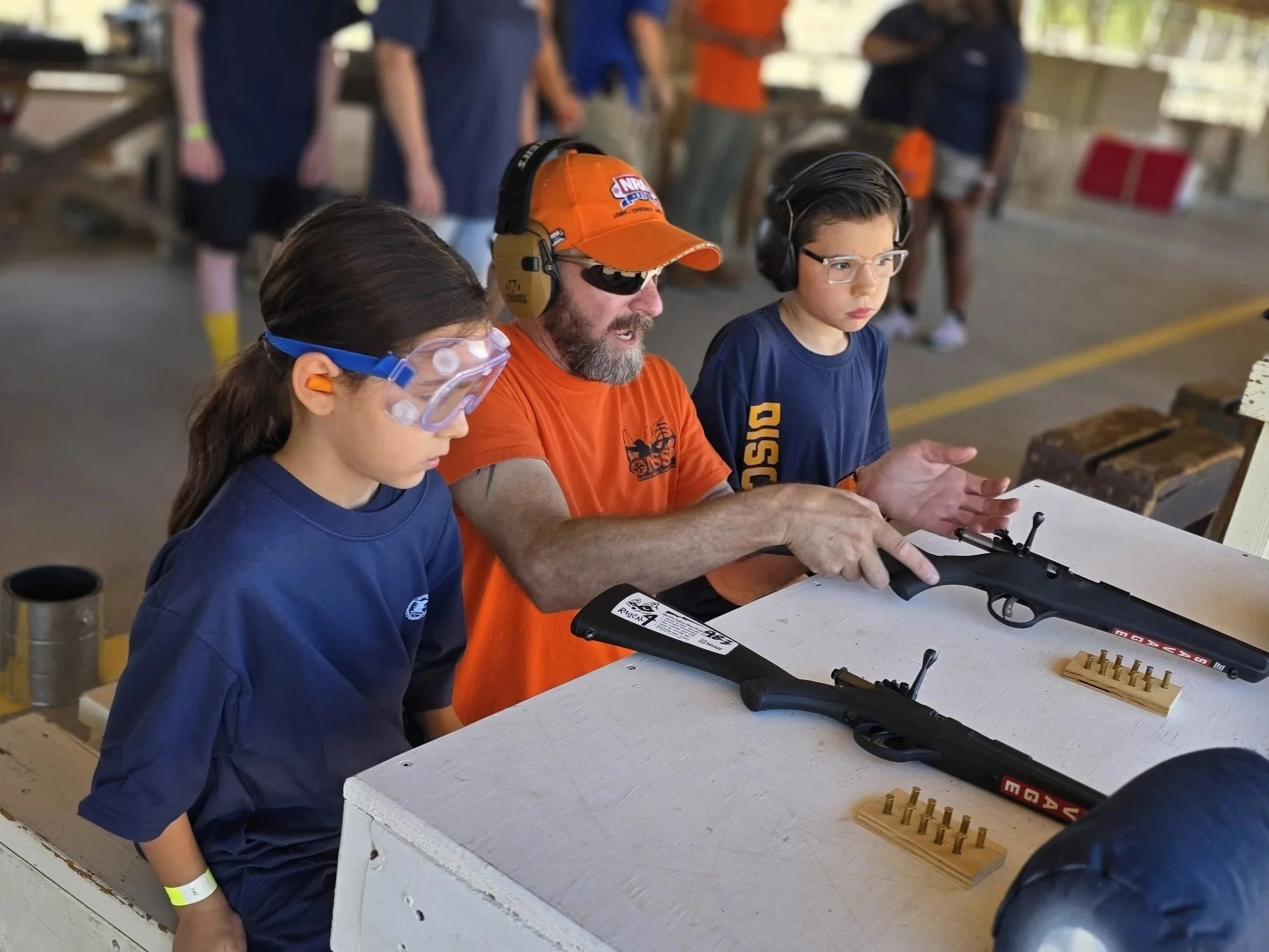Two Royal Rangers and a Commander at a shooting range, with rifles and safety gear, learning about shooting.