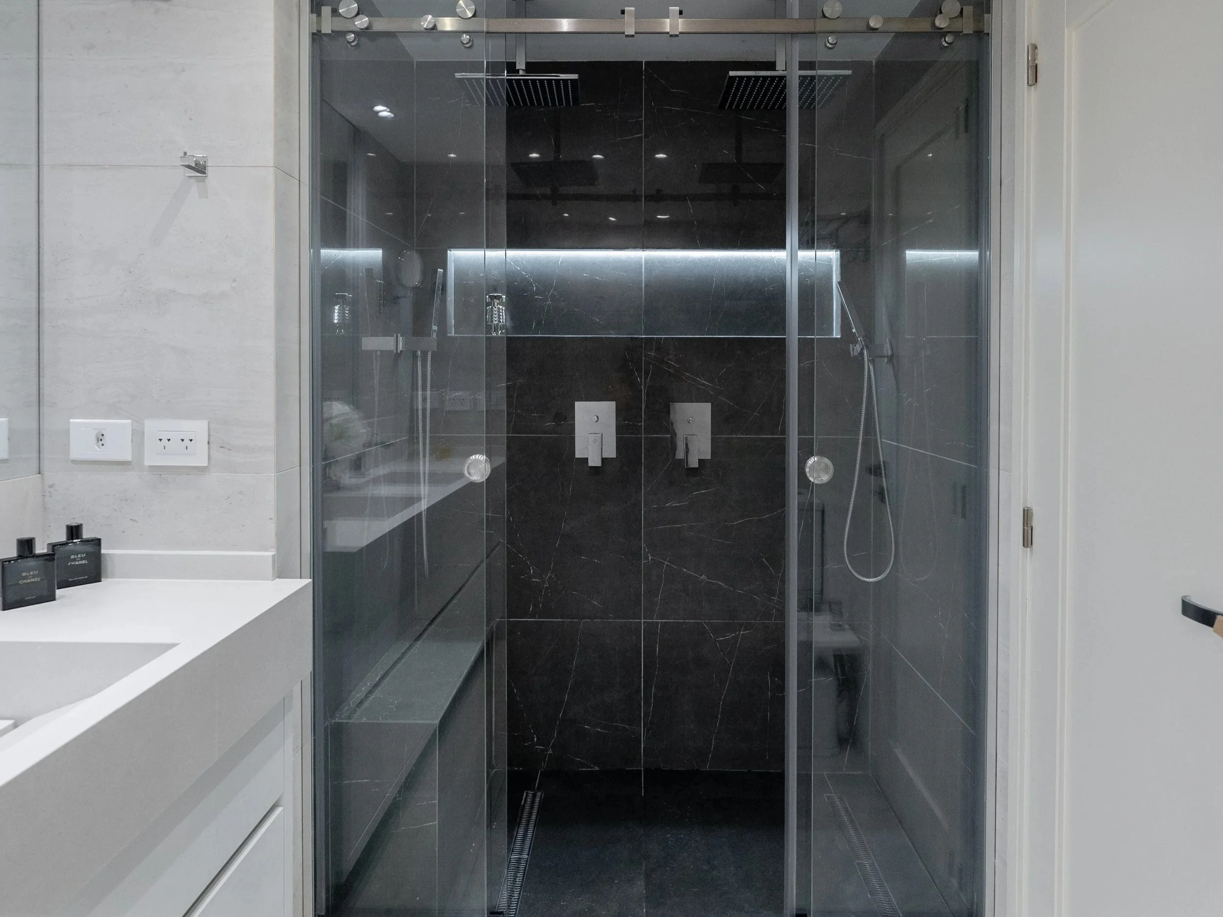 Ducha moderna con paredes de mármol negro, puertas de vidrio y accesorios de ducha en un baño de diseño contemporáneo.