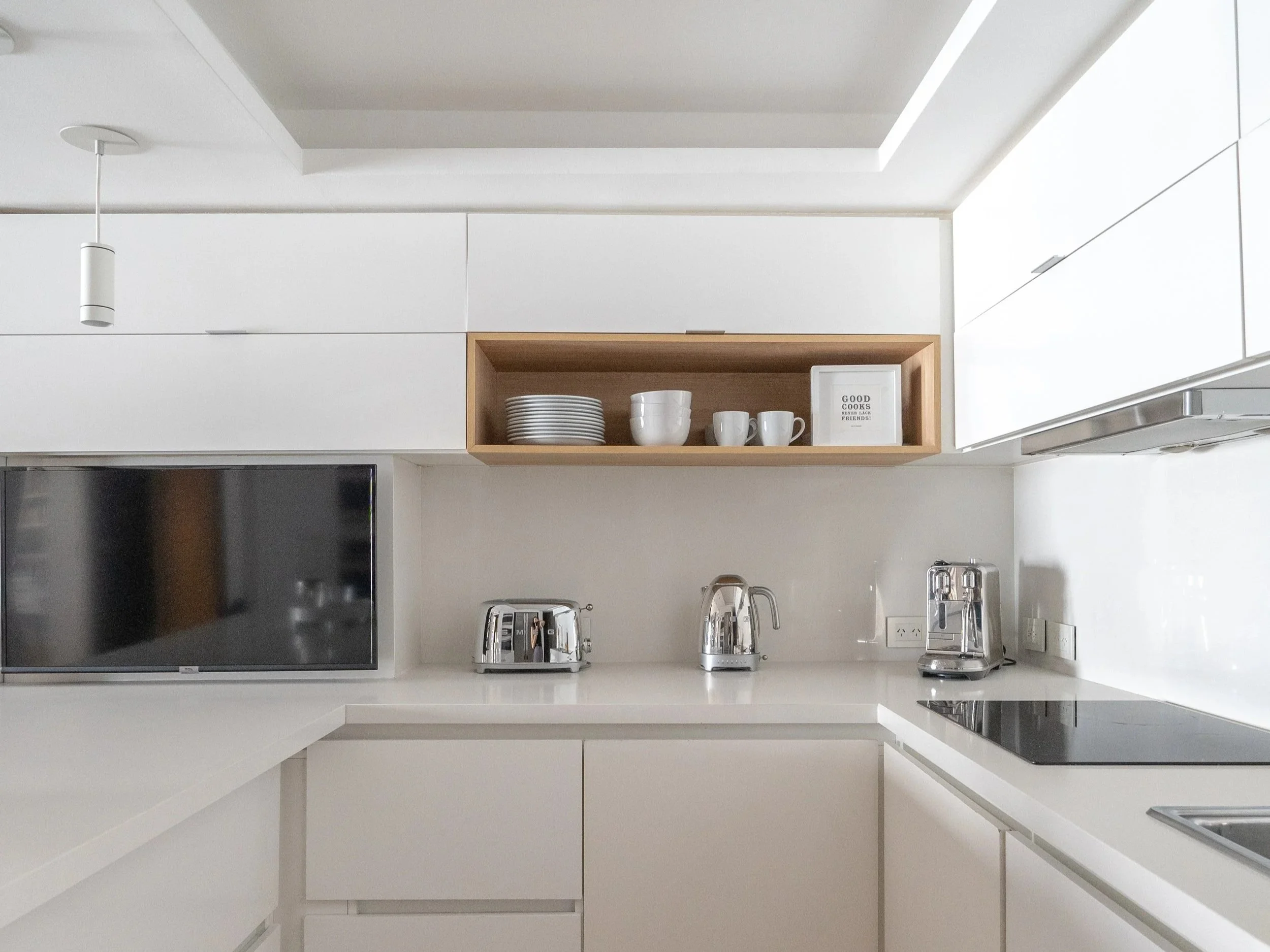 Cocina moderna con electrodomésticos de acero inoxidable, estantes blancos, y vajilla blanca en una repisa de madera.