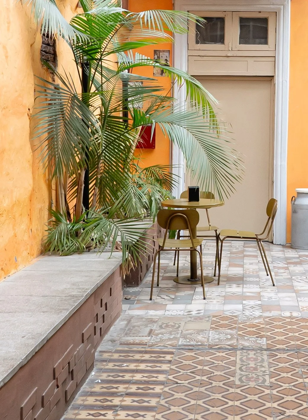 Piso decorativo de azulejos, mesa con sillas y plantas en un espacio interior con paredes de color naranja y detalles blancos.