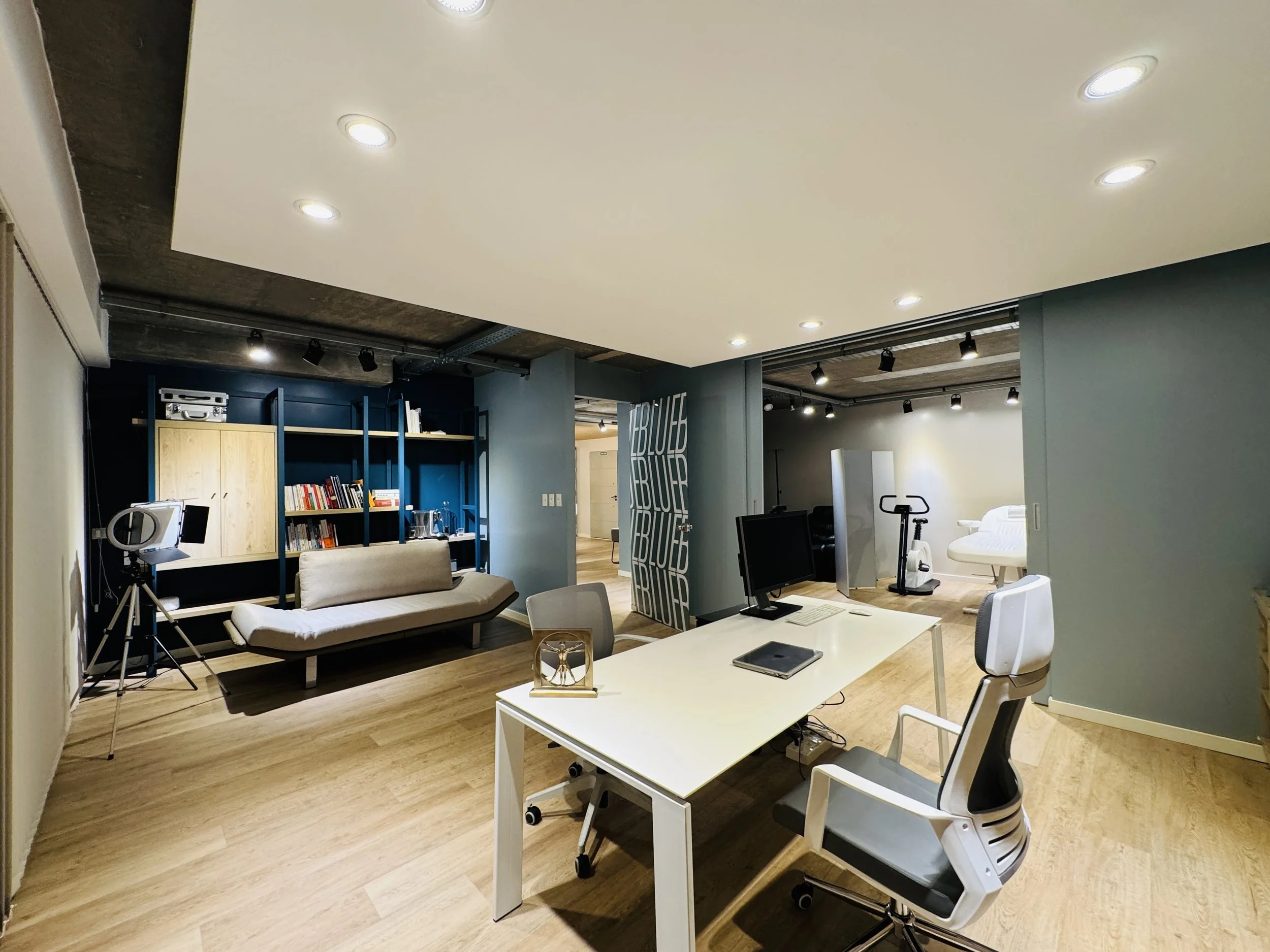 Oficina moderna con escritorio, silla, estantería con libros, sofá y área de ejercicio