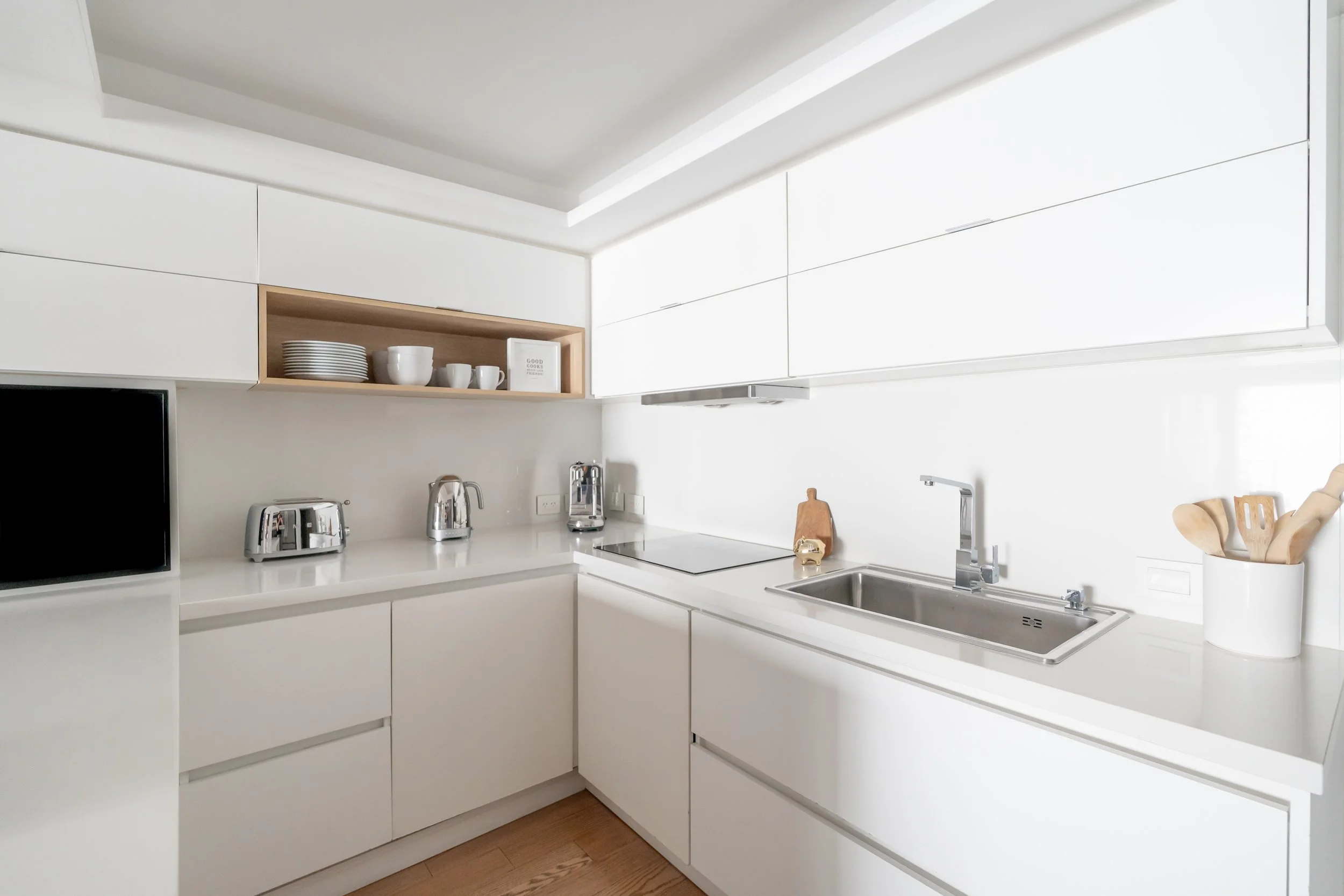 Cocina moderna y minimalista con gabinetes blancos, electrodomésticos de acero inoxidable y utensilios de madera.