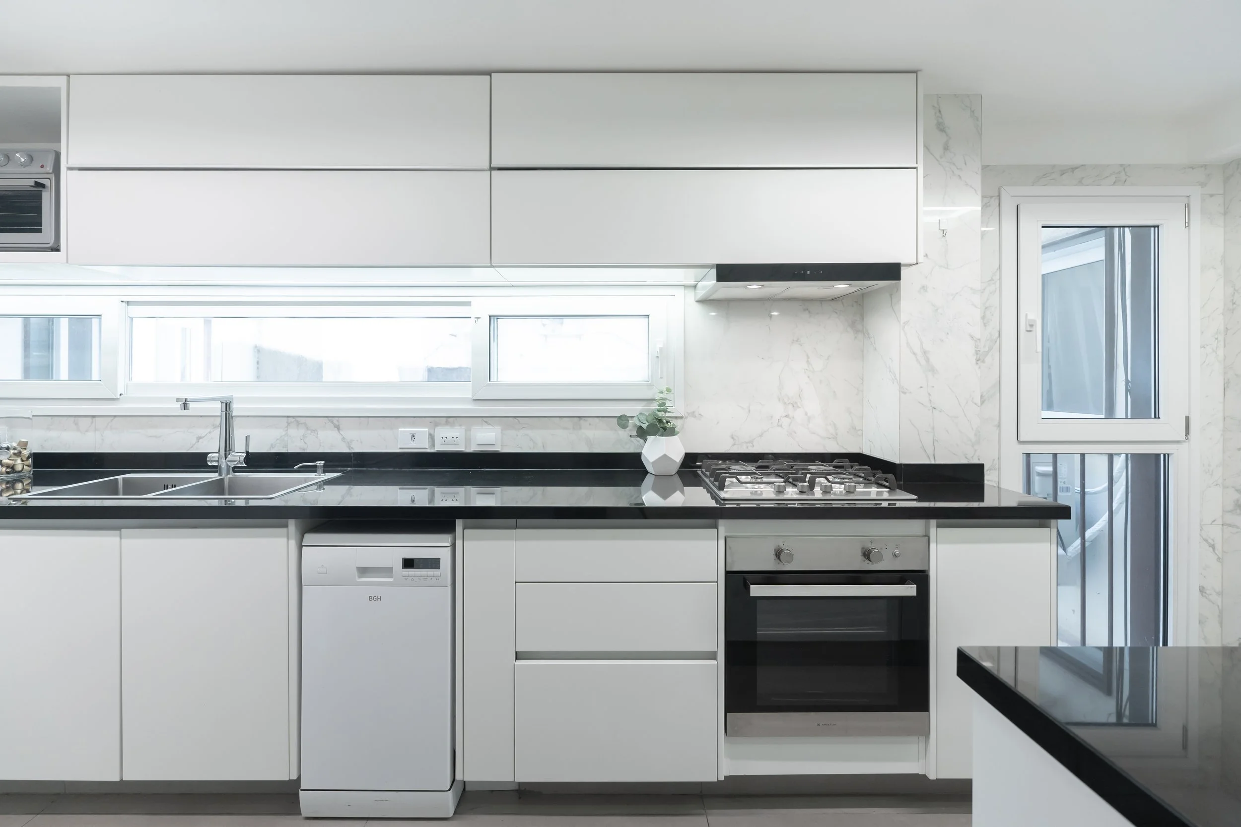 Cocina moderna con gabinetes blancos, encimera negra, horno, estufa de gas, ventana y puerta de vidrio.