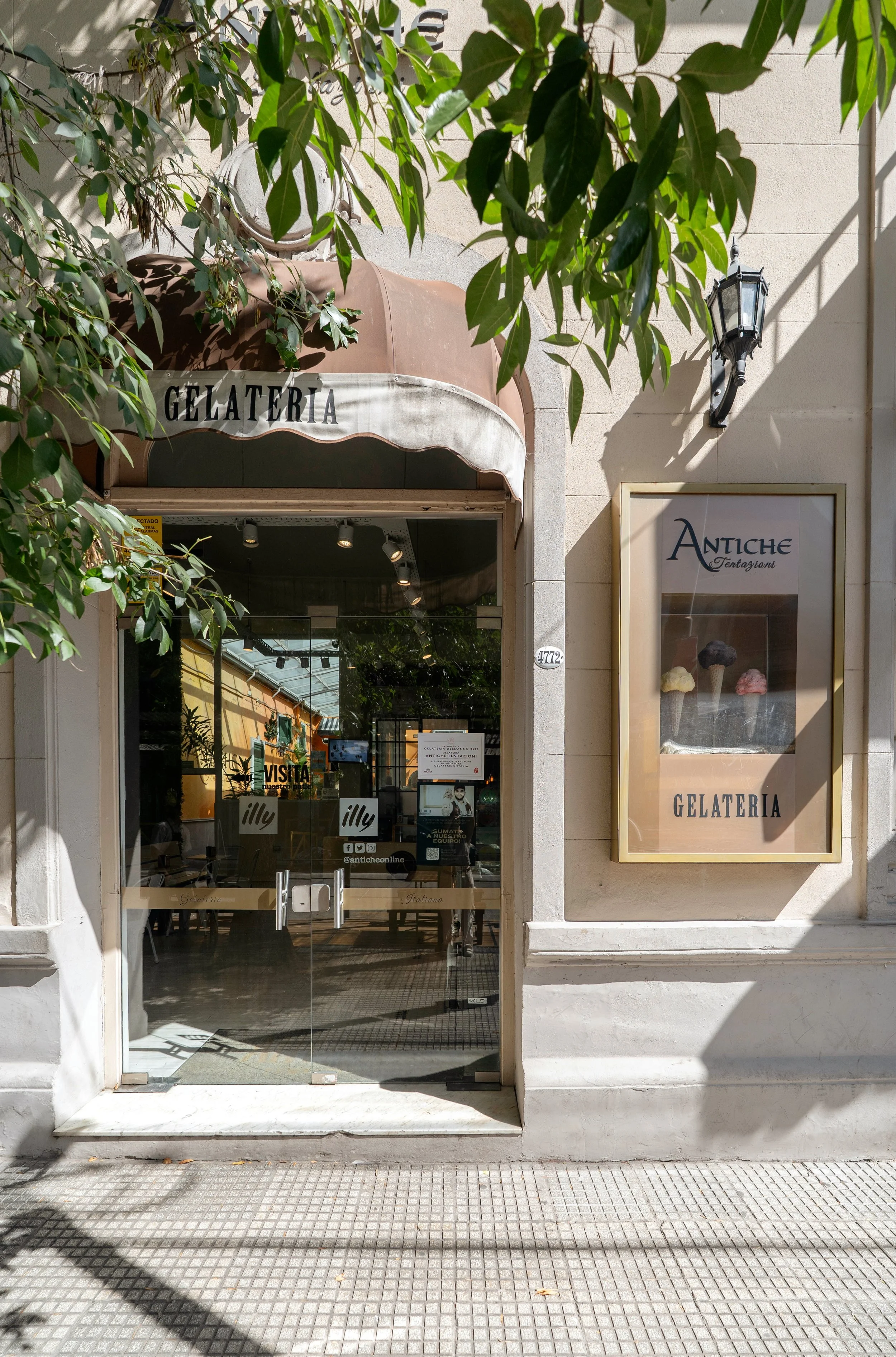 Fachada de una heladería llamada Antiche, con la palabra 'GELATERÍA' en un cartel y en la marquesina. Puerta de cristal con letreros y logotipos.