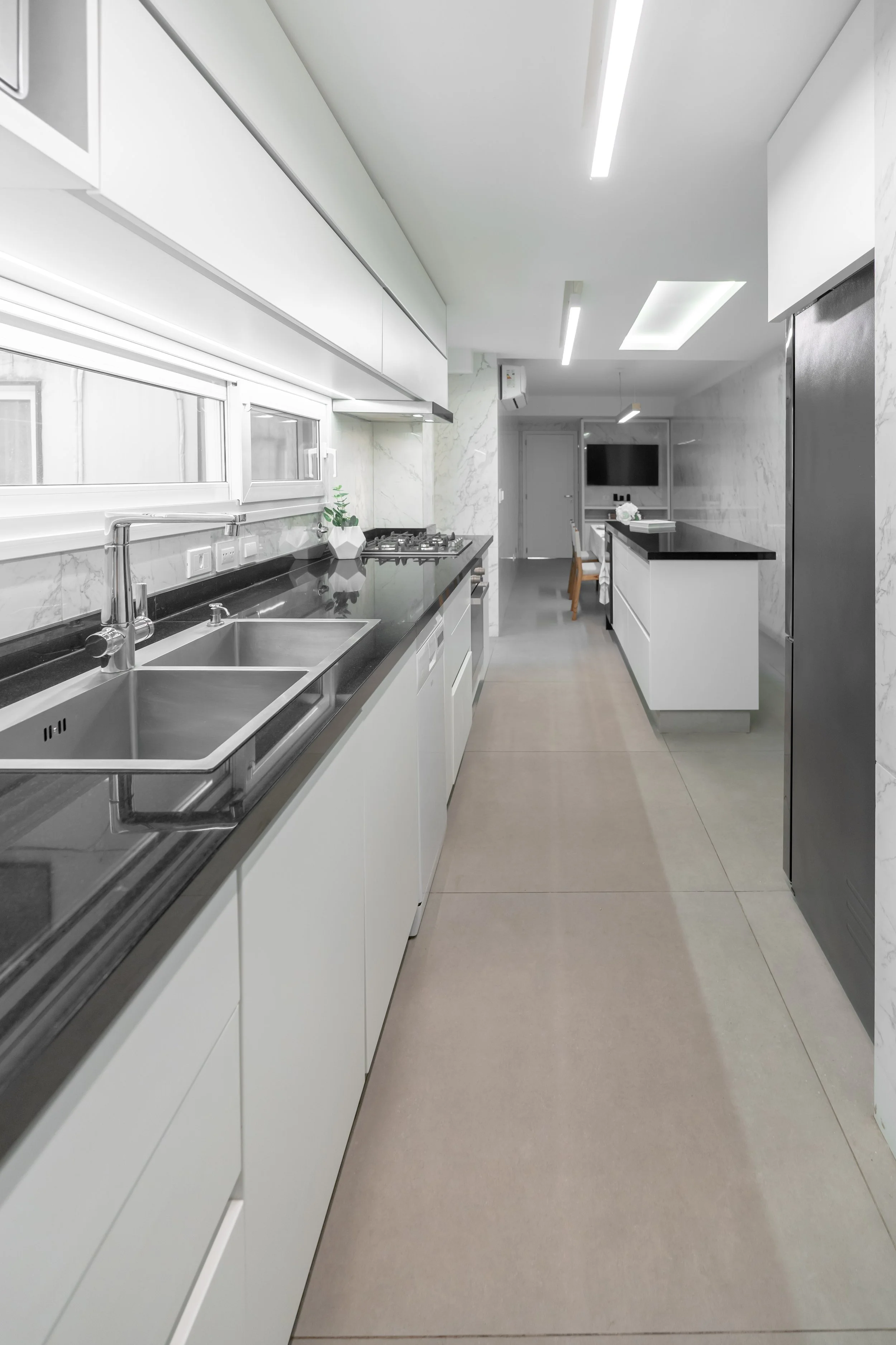 Cocina moderna con encimeras negras, fregadero doble, ventana, y decoraciones minimalistas en tonos blancos y grises.