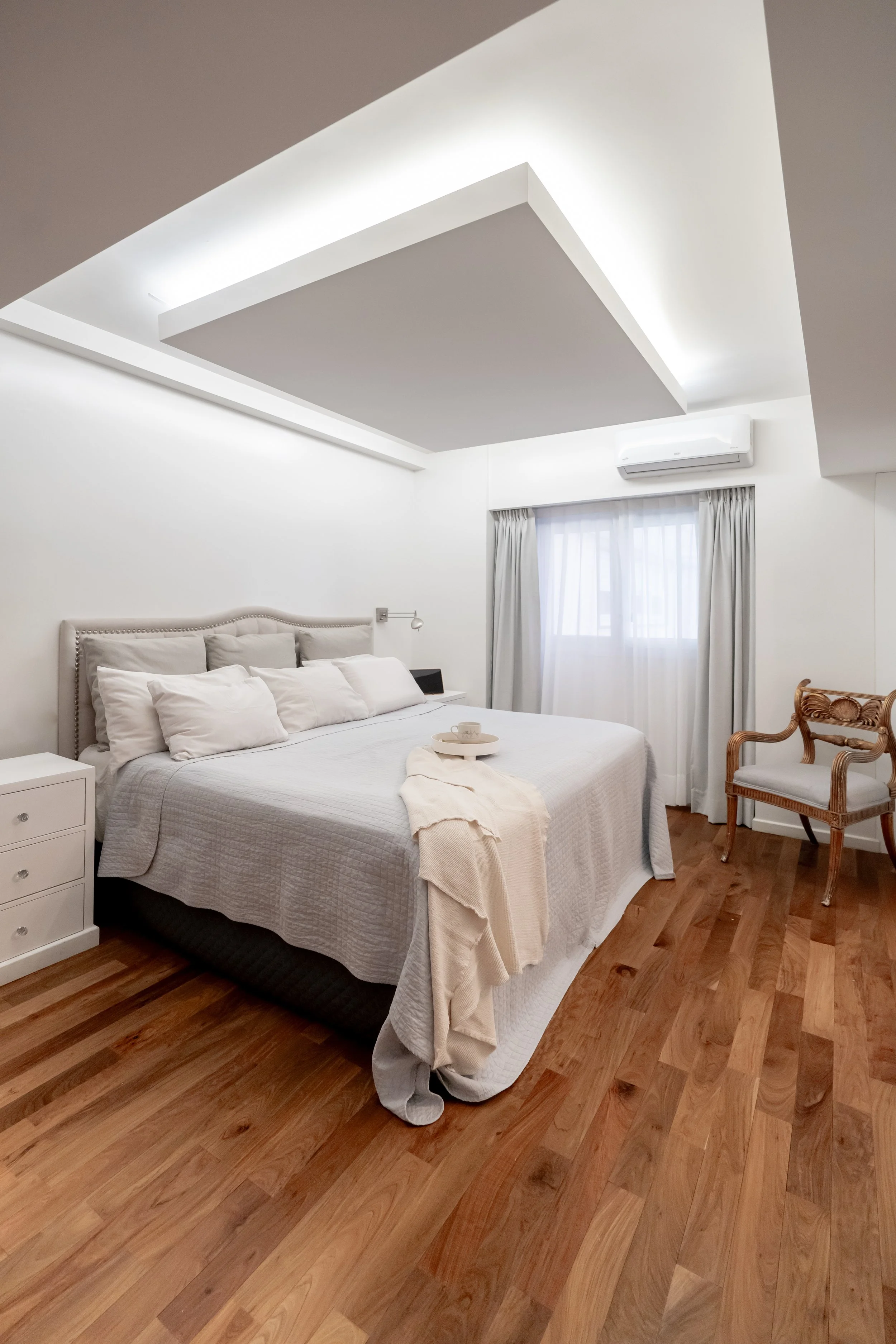 Habitación moderna con cama grande, ropa de cama blanca, ventanas con cortinas blancas, suelo de madera y decoraciones minimalistas.