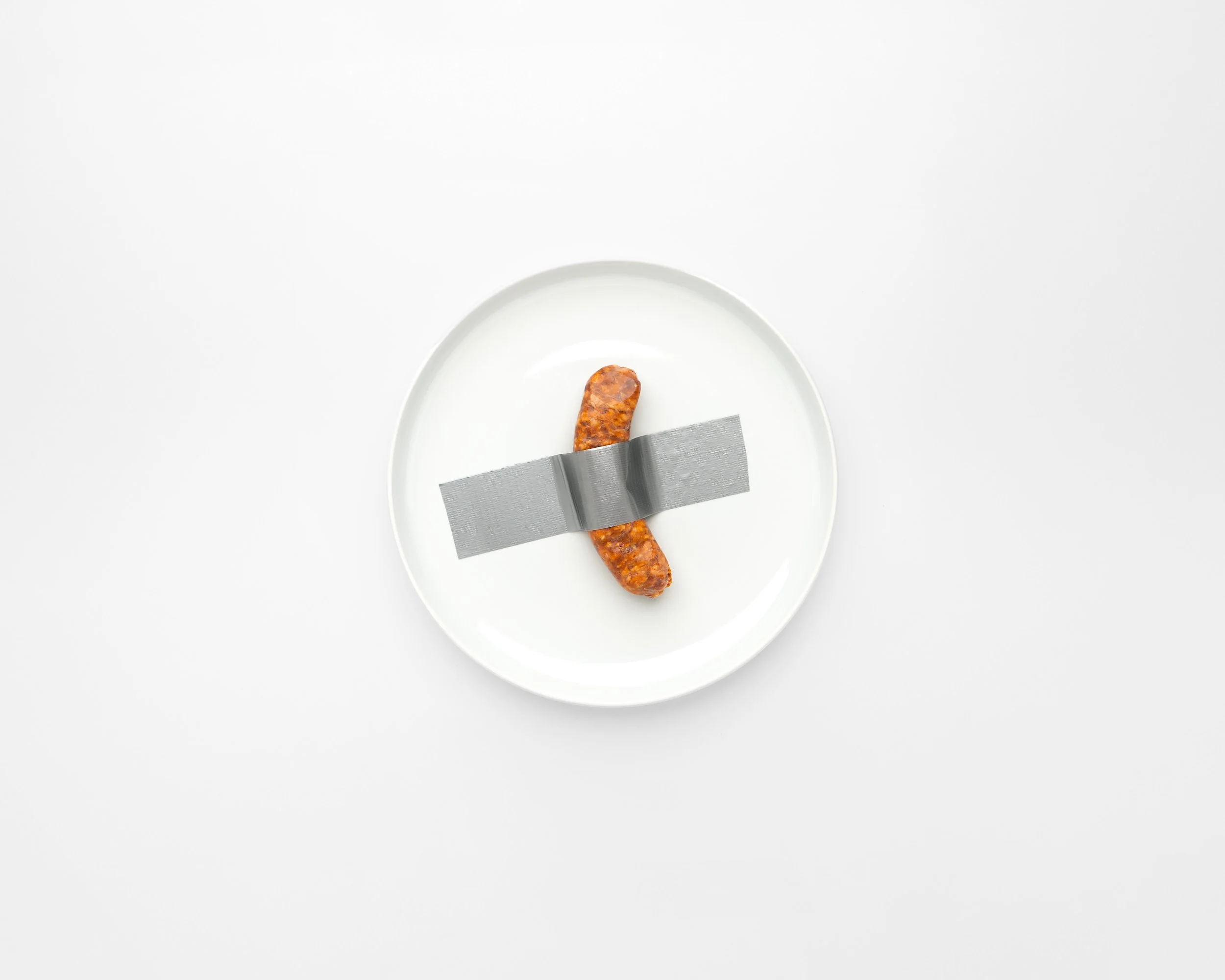 Single sausage link on a white plate, secured with gray duct tape, on a white background.