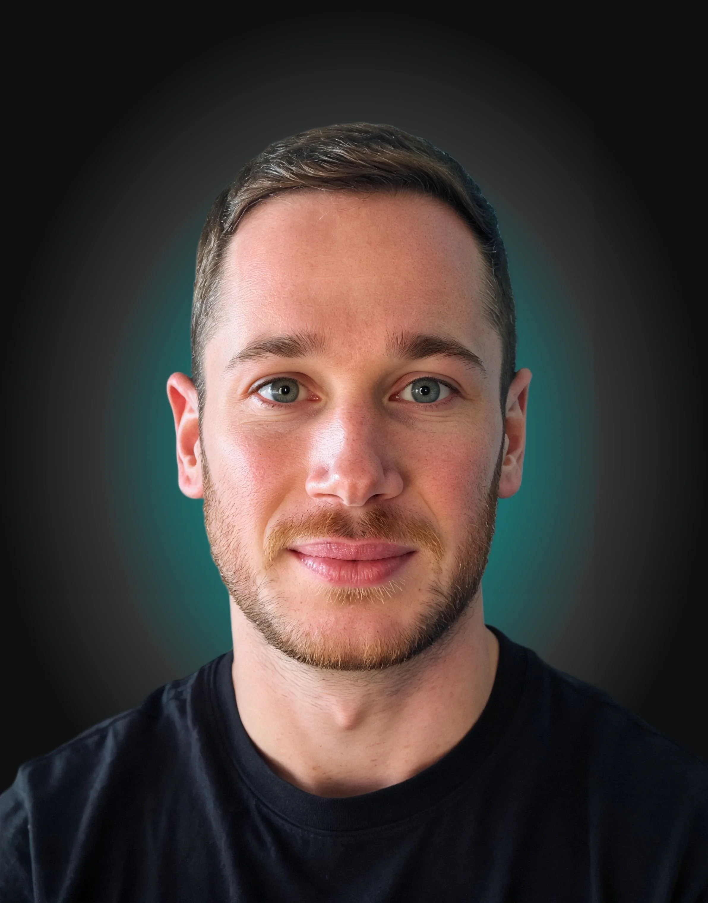 Close-up portrait of a young man with fair skin, blue eyes, light brown hair, and a short beard, wearing a black t-shirt, against a dark background with a faint teal glow.