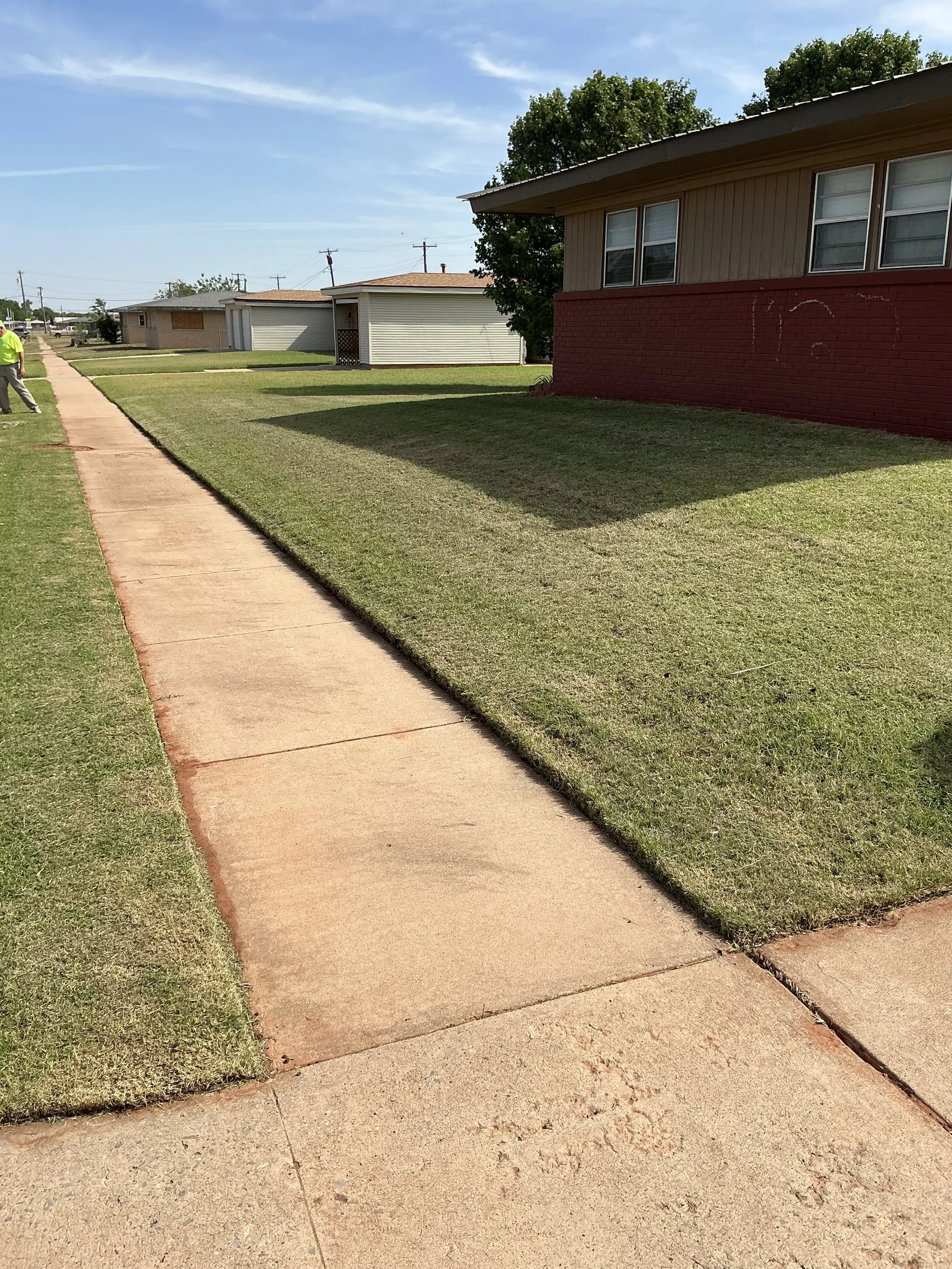 A sidewalk running through a grassy lawn in front of residential houses with clear blue skies overhead.