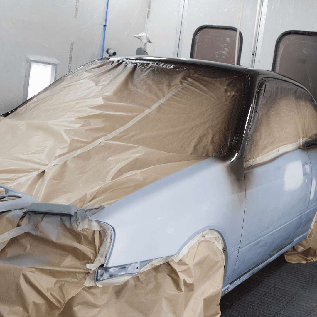 A car being painted in an auto body shop with masking paper covering the windows and parts of the car.