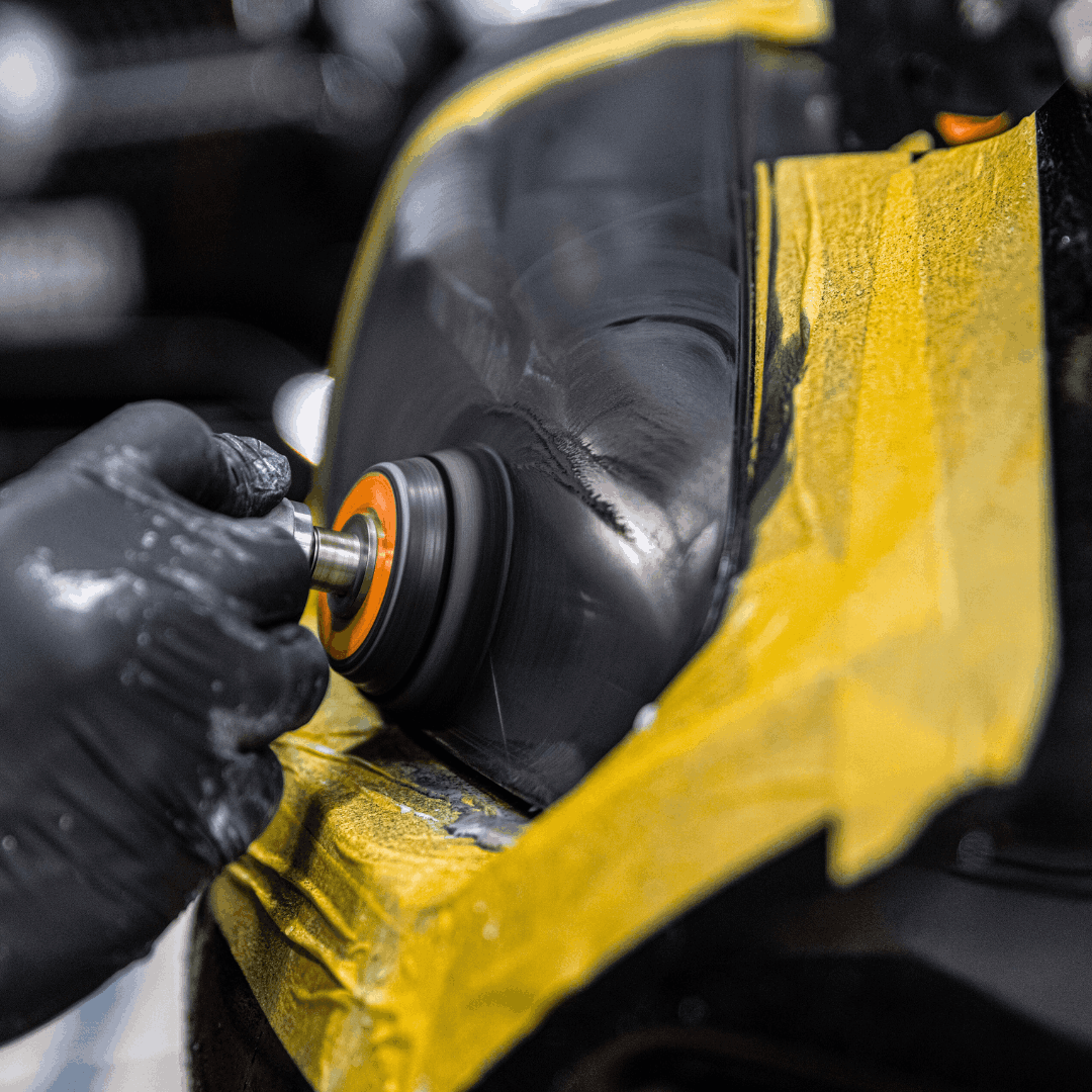 A person wearing black gloves is polishing or grinding a black disc or wheel with an orange and silver tool.